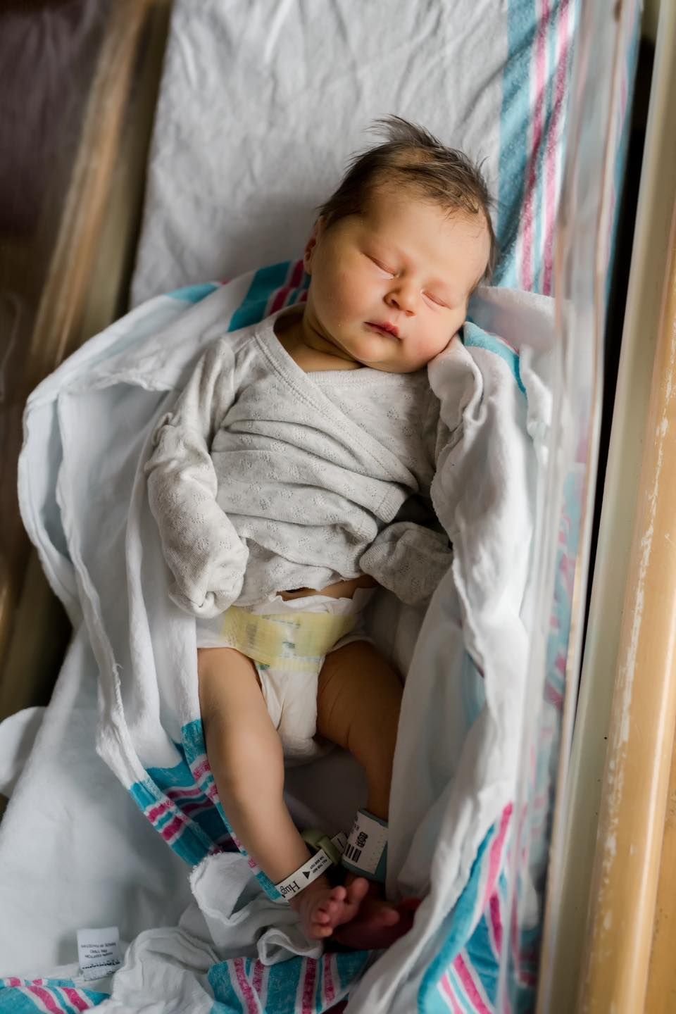 Sleeping baby wearing white clothes rests peacefully in a crib.