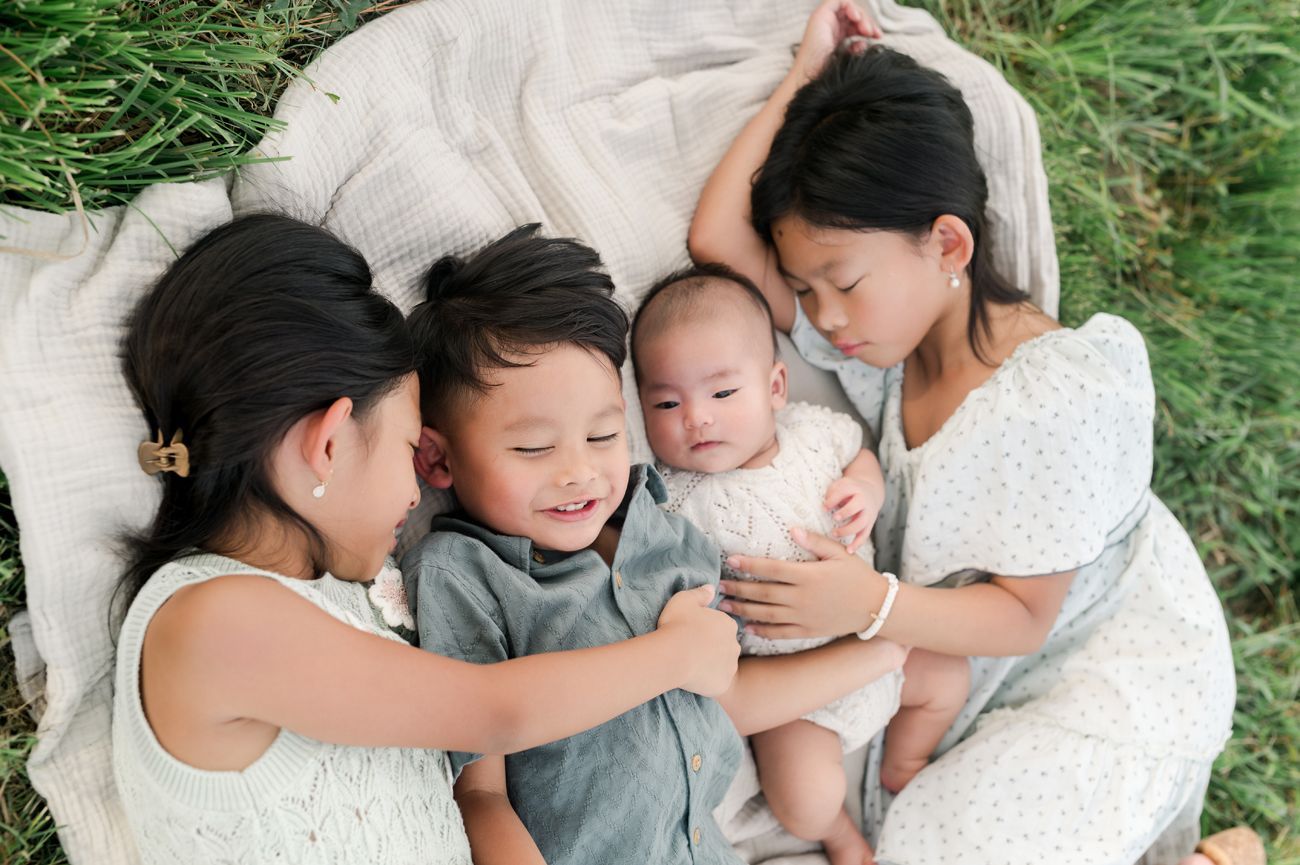 Family cuddles together on white bedding during intimate lifestyle photo session.