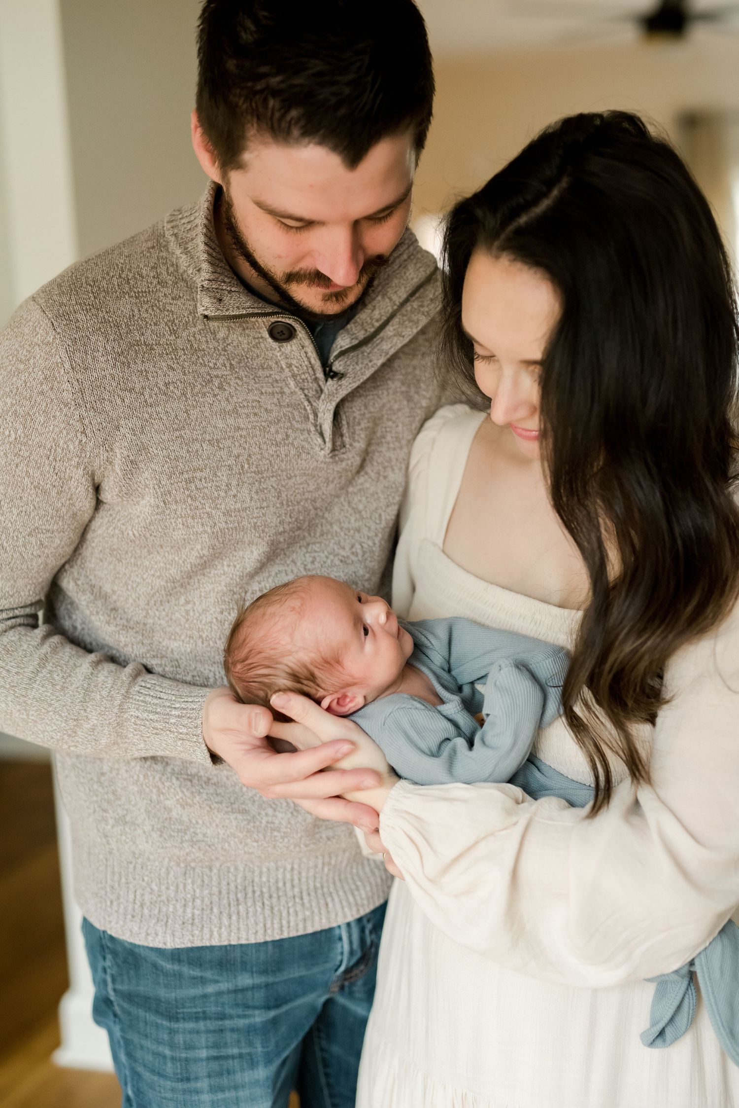 Parents in casual attire holding newborn baby in indoor setting.