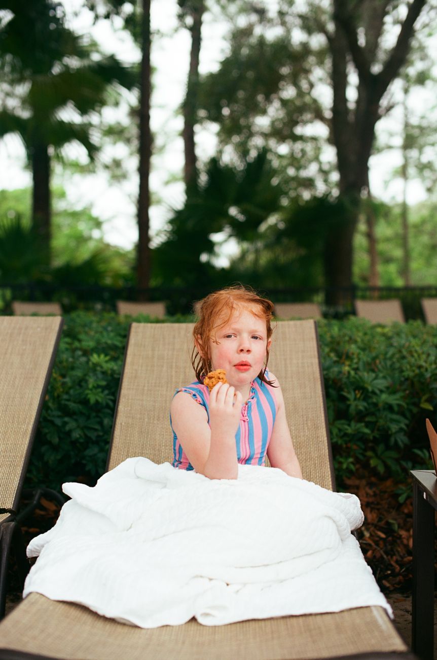 A young child wrapped in white bedding rests on a lounge chair outdoors.