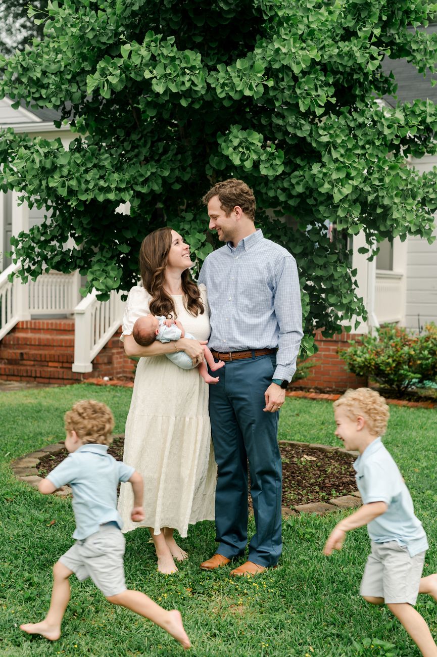 A family enjoys a playful moment together on their front lawn with children running around on a sunny day.