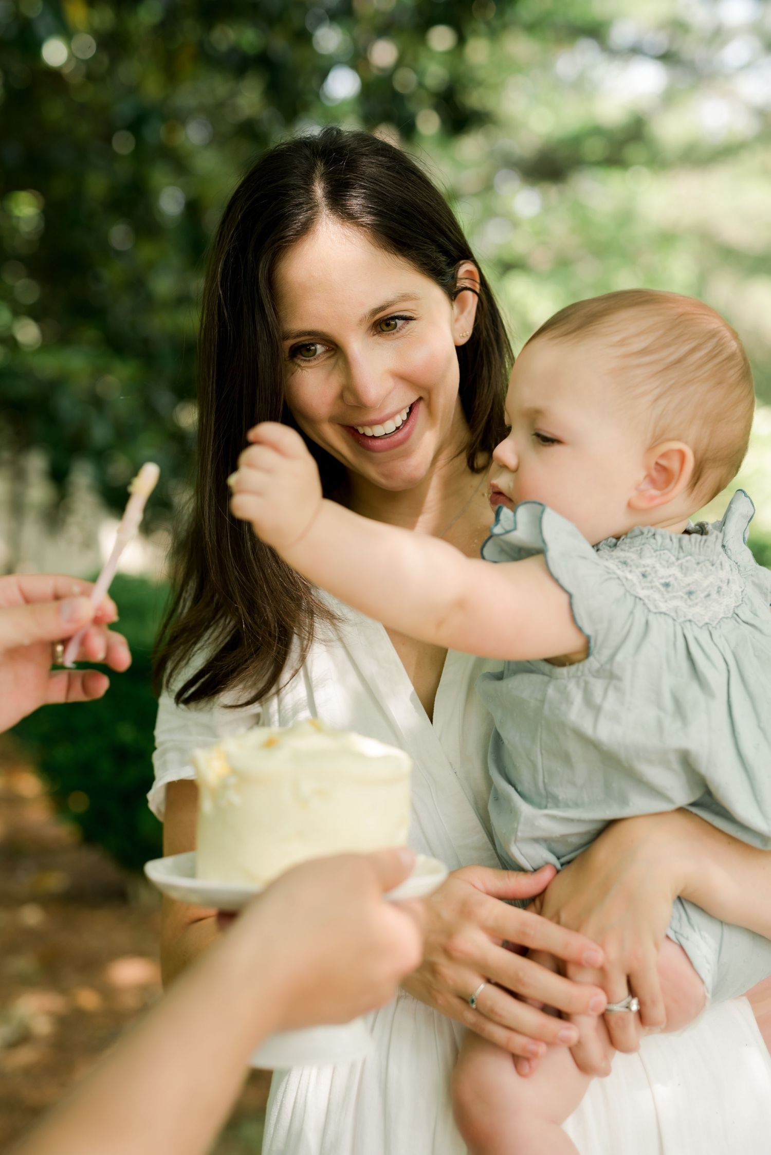 Happy moment sharing cake outdoors with baby in white dress.