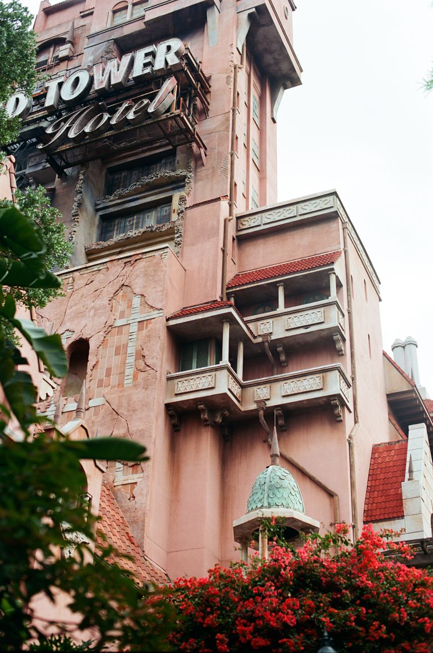 Pink Tower of Terror building facade with ornate architectural details and blooming red flowers at Disney World.
