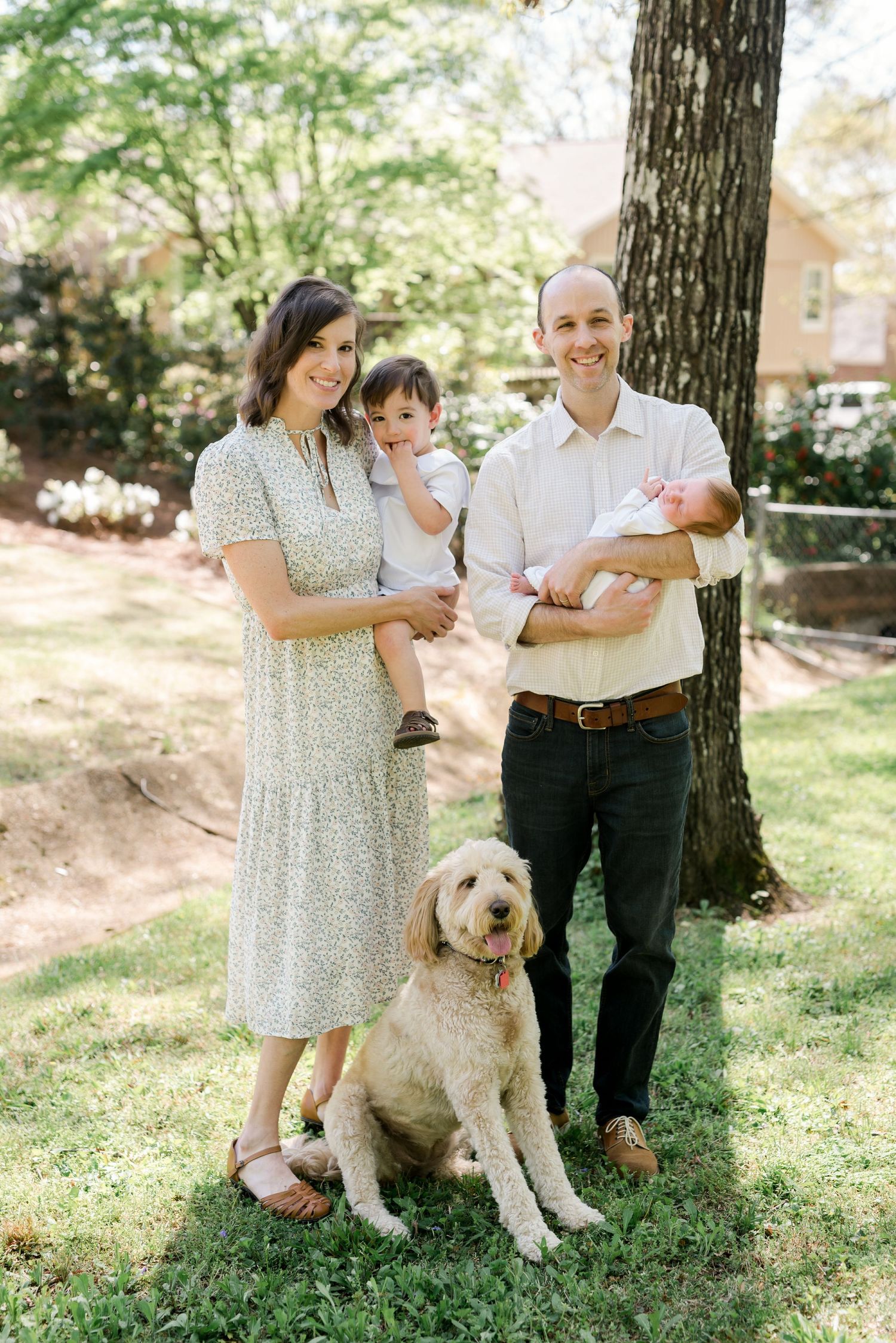 Family portrait outdoors with a goldendoodle dog under a tree on a sunny day.