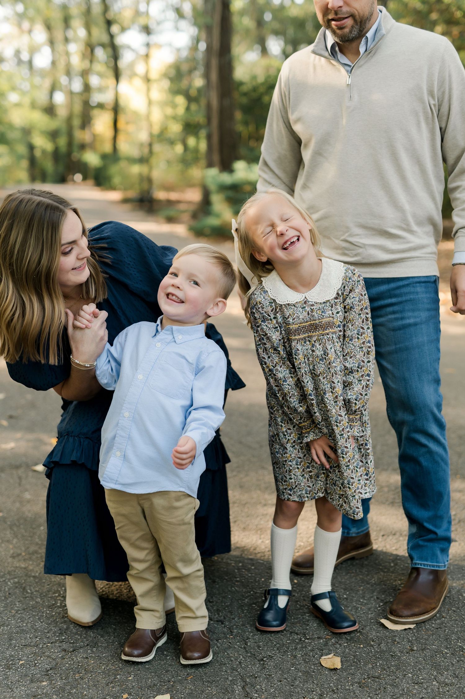 A joyful family of four laughing together outdoors on a wooded path during a fall family portrait session.
