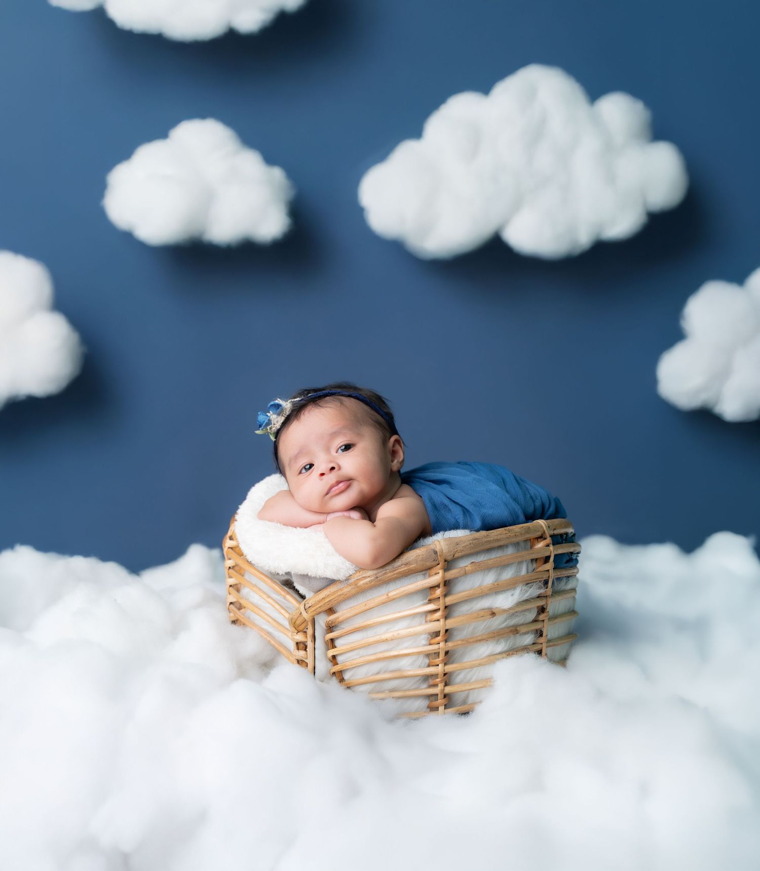 Whimsical newborn photo setup with cotton cloud backdrop and wooden basket prop.