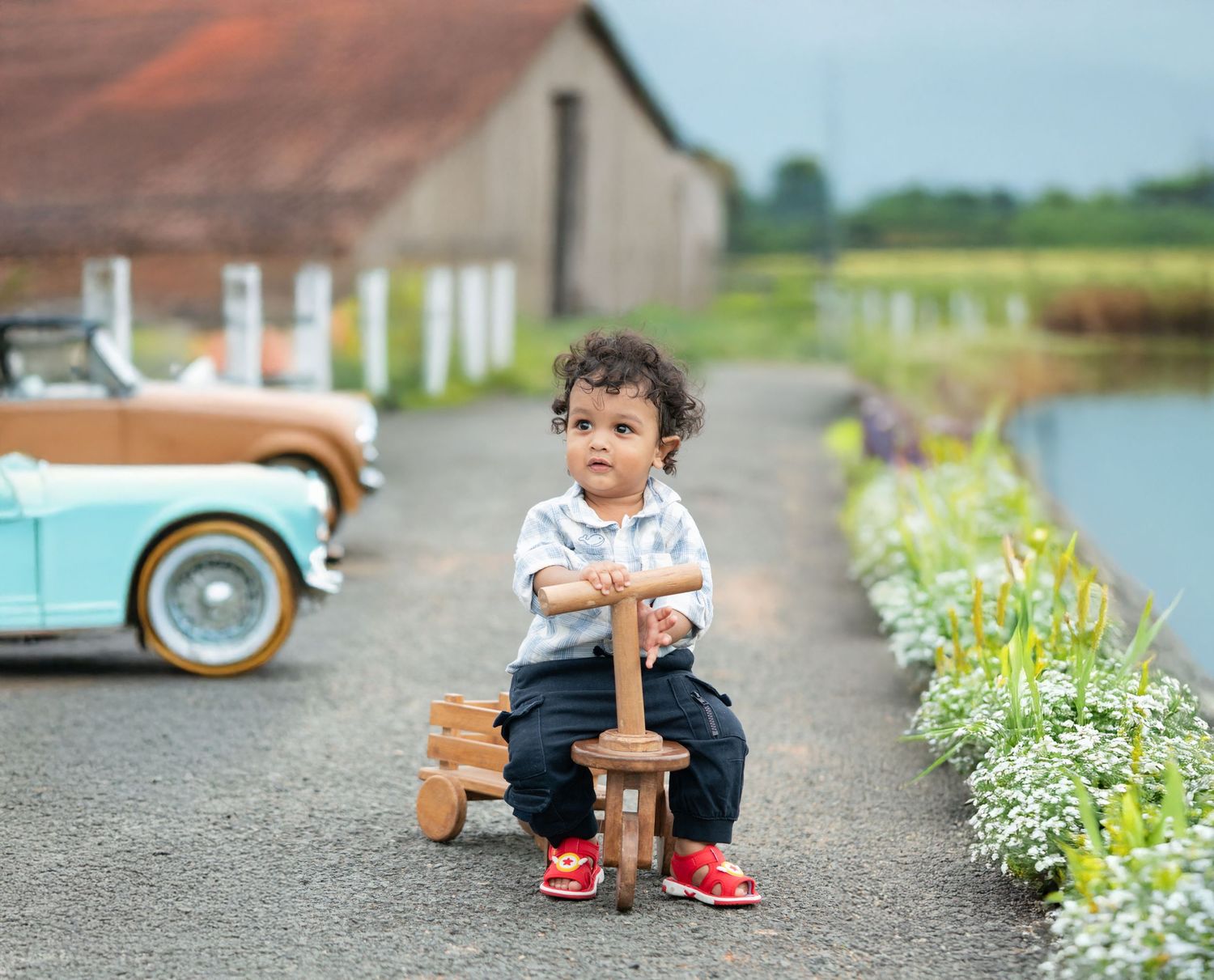 Child rides wooden rocking horse on path with vintage car in background.