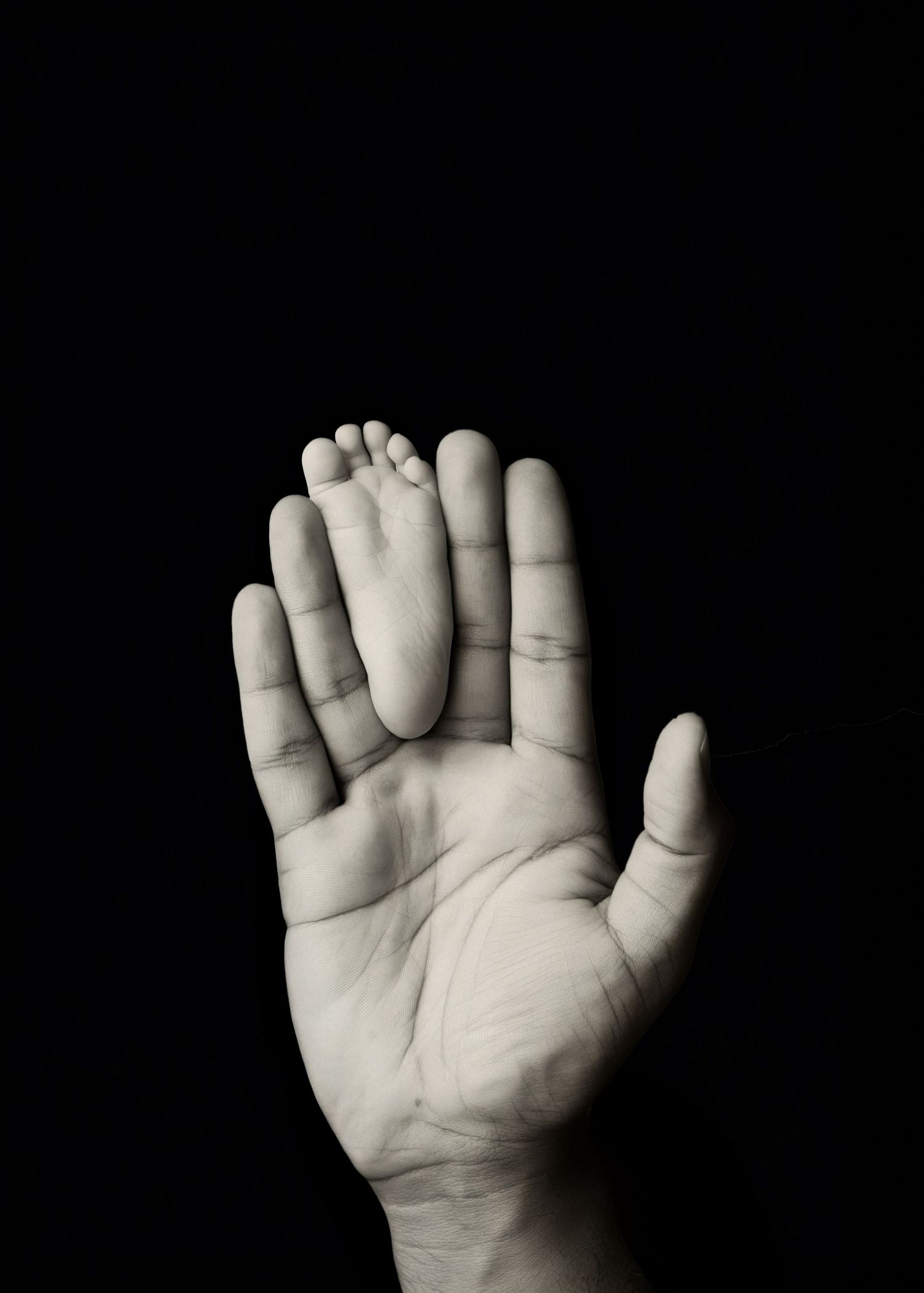 Black and white close-up study of tiny infant hands against dark background.