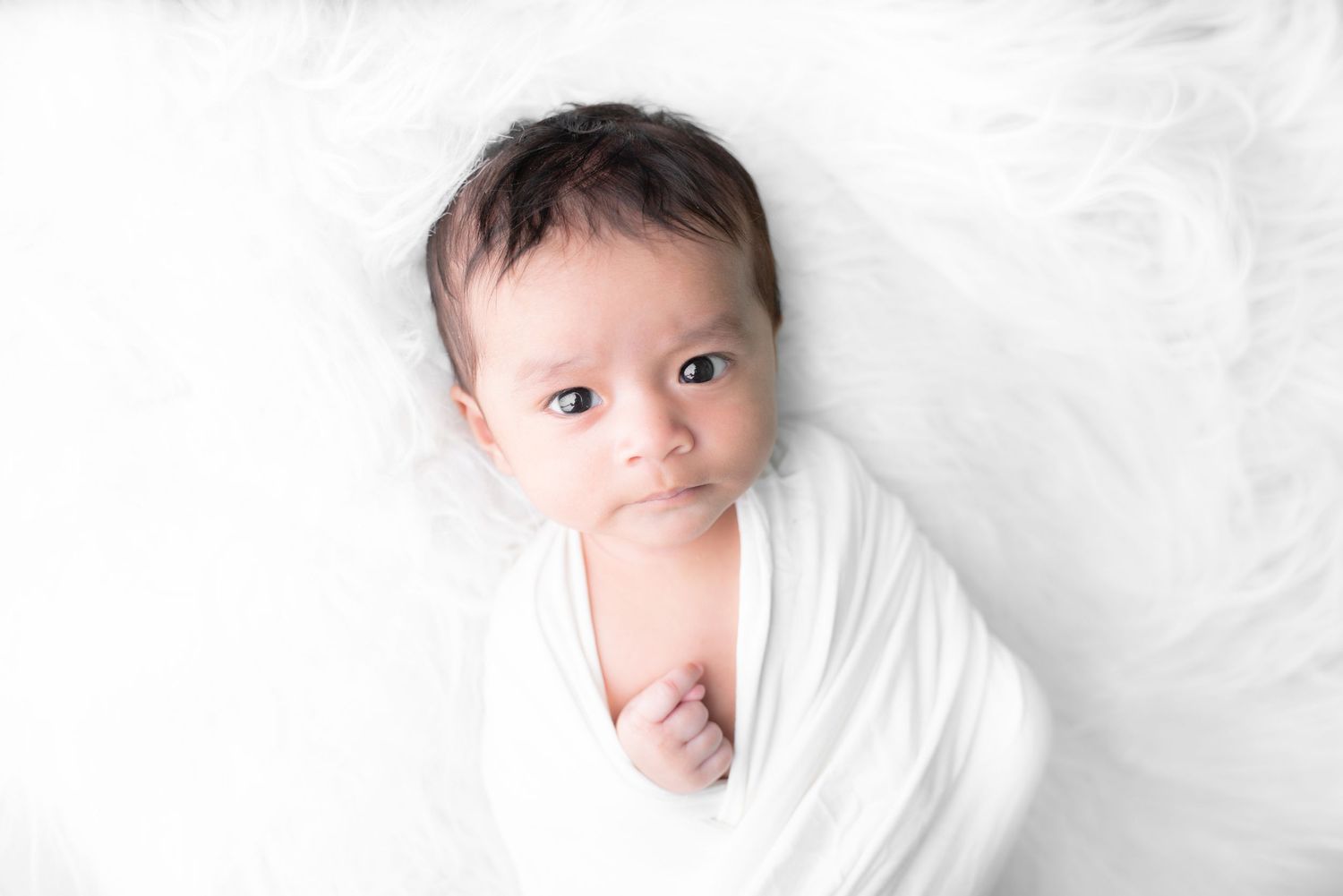 Minimalist white-on-white newborn portrait series with soft natural lighting.