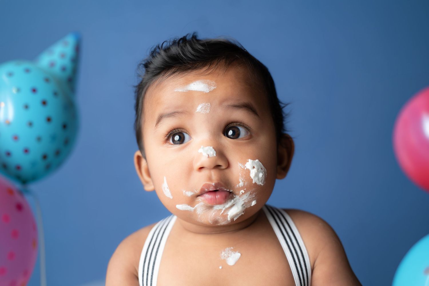 Cake smash photography session against blue backdrop with colorful polka dot decorations.