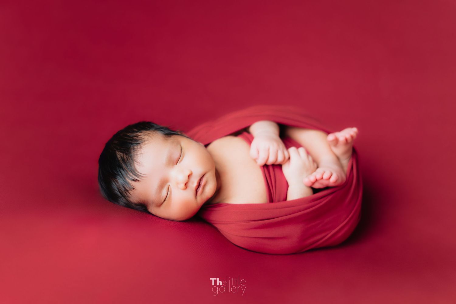 Minimalist newborn photography against deep red background.