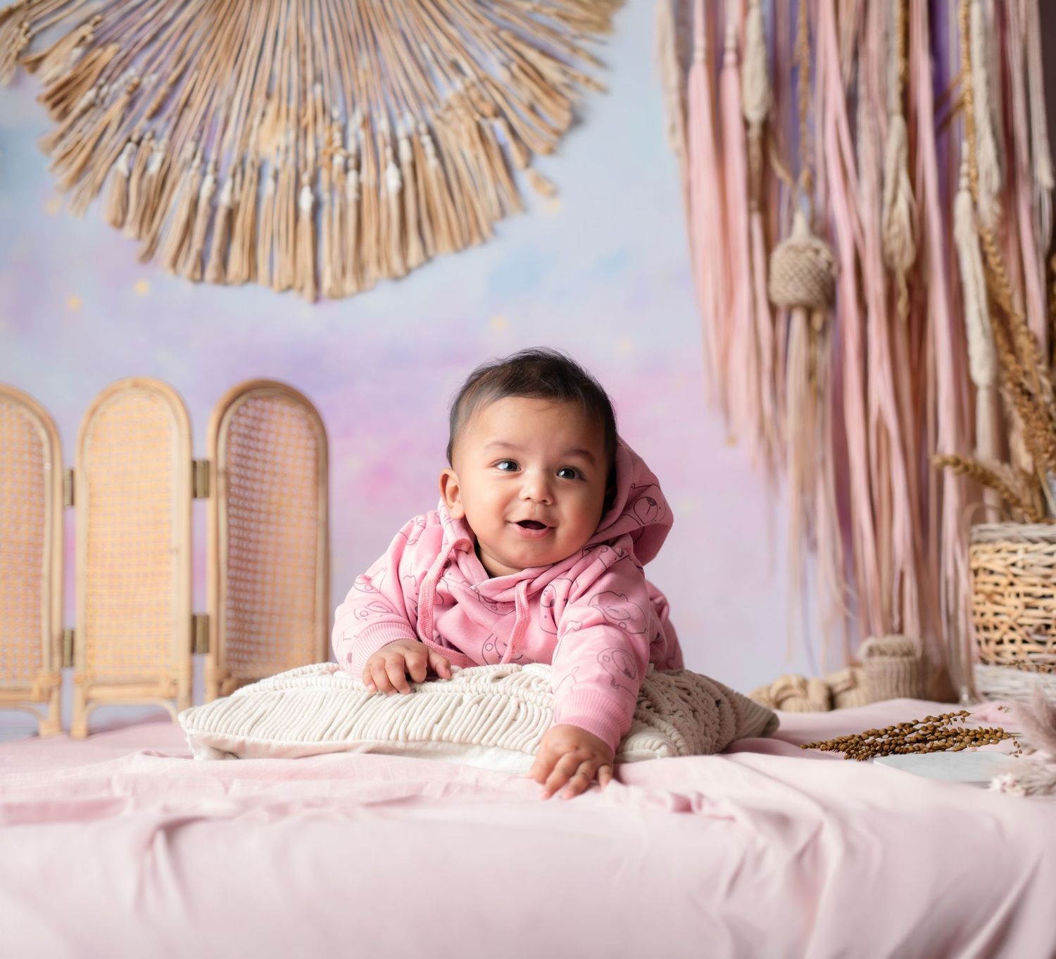 Baby milestone photos with boho decor featuring pink accents and sunburst wall art.