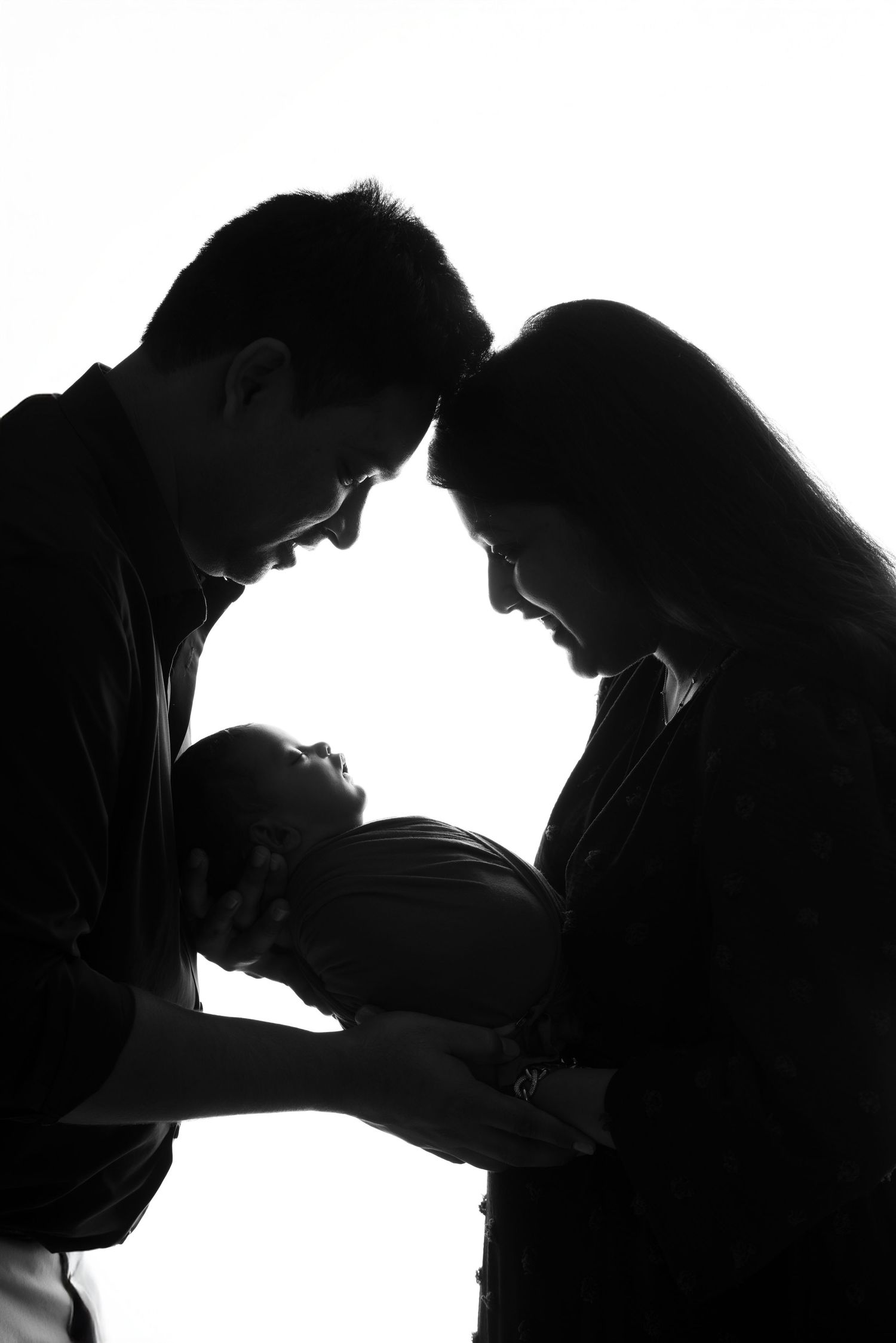 Silhouette of parents looking down lovingly at their newborn baby in dramatic lighting.