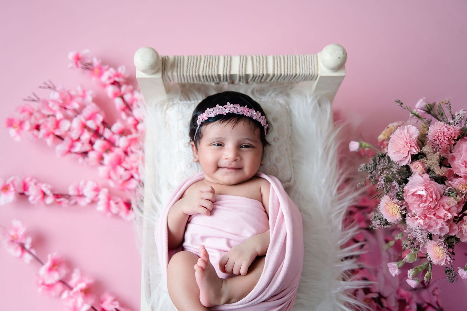 Pink floral newborn photography setup with delicate cherry blossoms and soft textures.