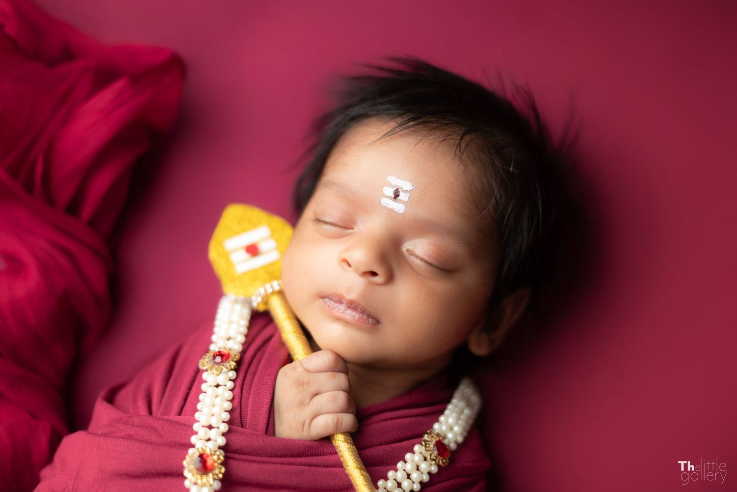 Artistic newborn photography session with deep red backdrop and traditional Indian accessories.