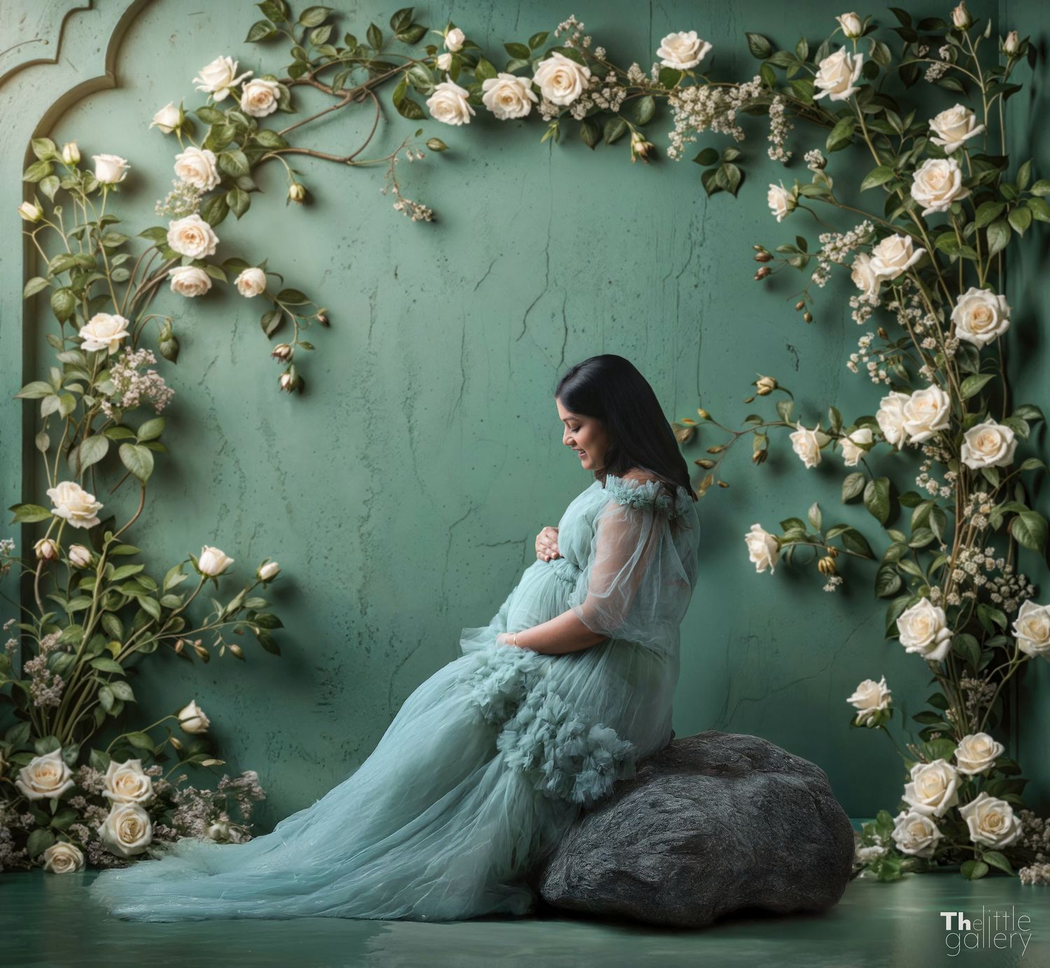 Ethereal maternity photoshoot with white roses and flowing blue gown against turquoise wall.