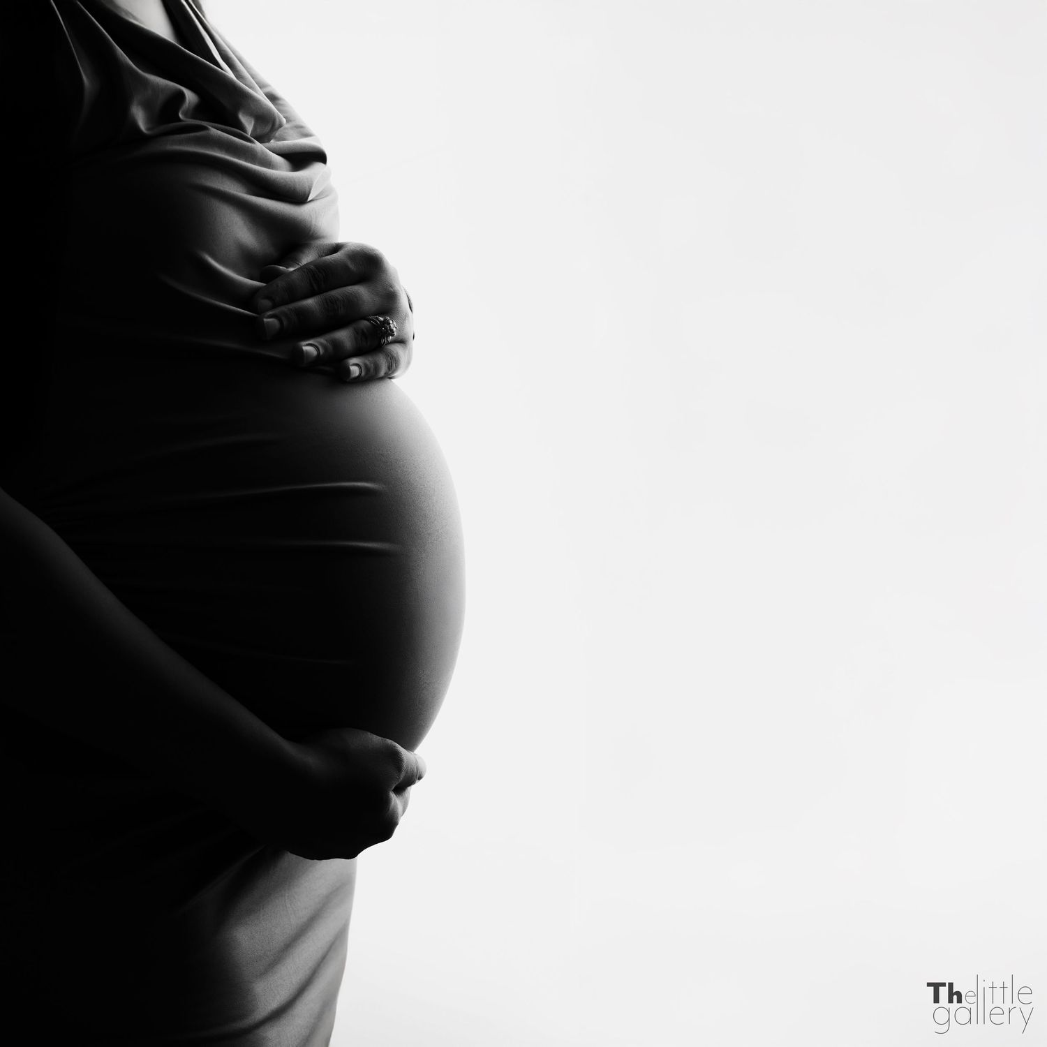 Artistic black and white silhouette of pregnant belly with hands gently resting on top.