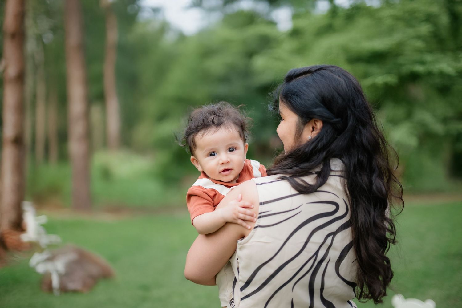 Mother and baby share tender moment in lush green forest setting.