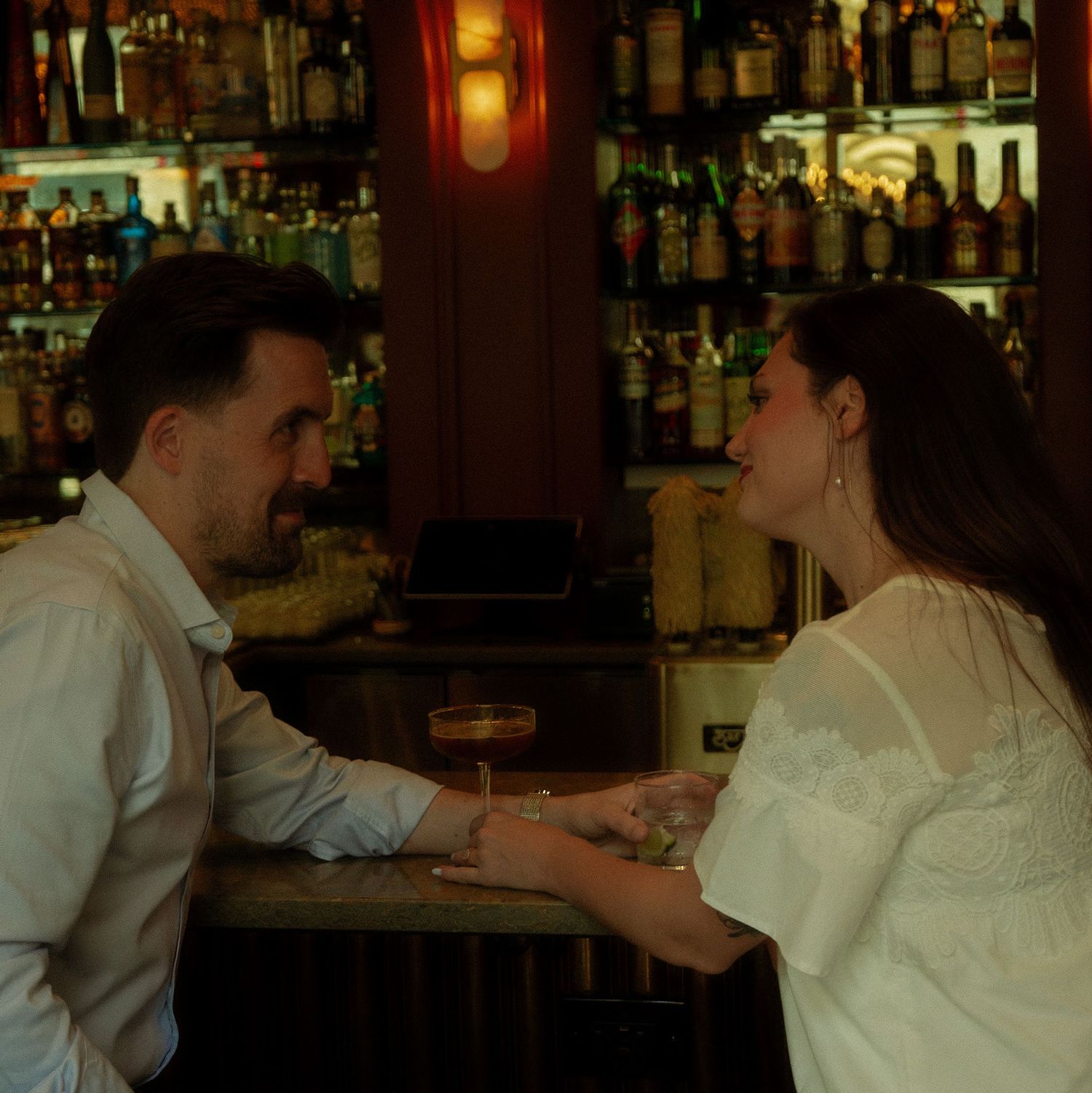 Couple sharing a romantic moment at a dimly lit bar with shelves of liquor bottles in the background.