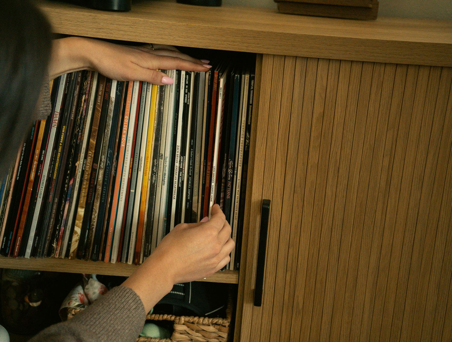 Person browsing a large collection of vinyl records stored vertically in a wooden cabinet shelf.