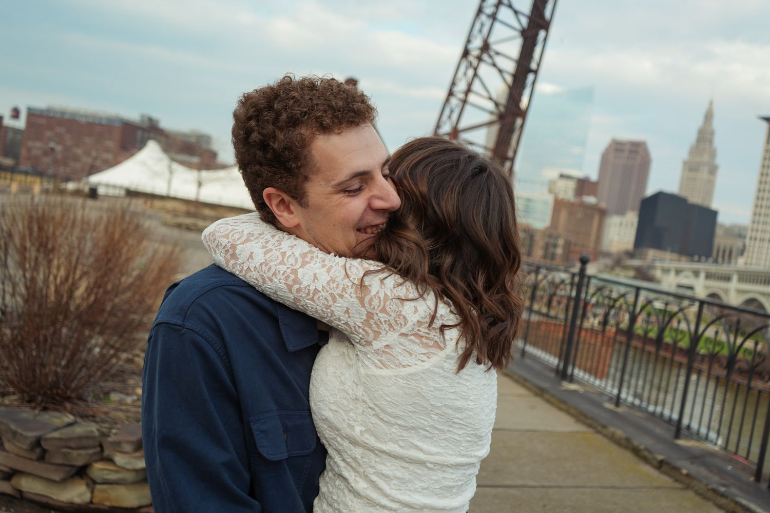 A couple embraces in front of a city skyline on an overcast day.