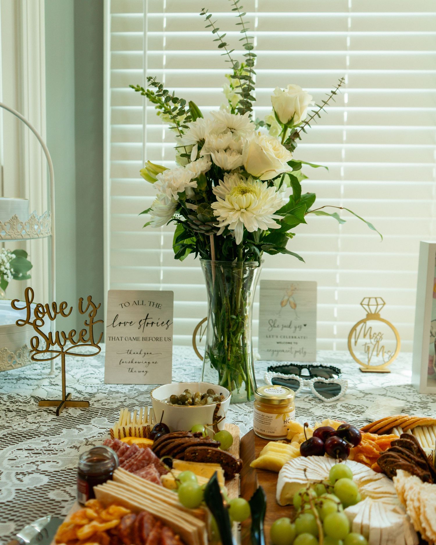 Elegant bridal shower table with white floral arrangement, charcuterie board, and gold Love is Sweet sign decor.