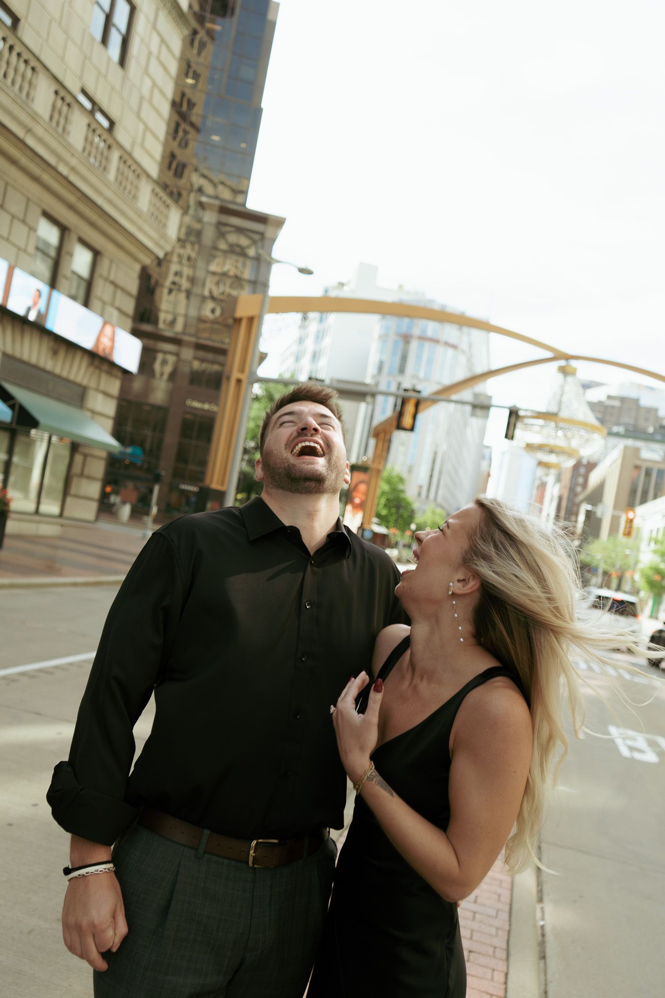 Laughing couple in matching black outfits enjoying a fun moment together on a city street.