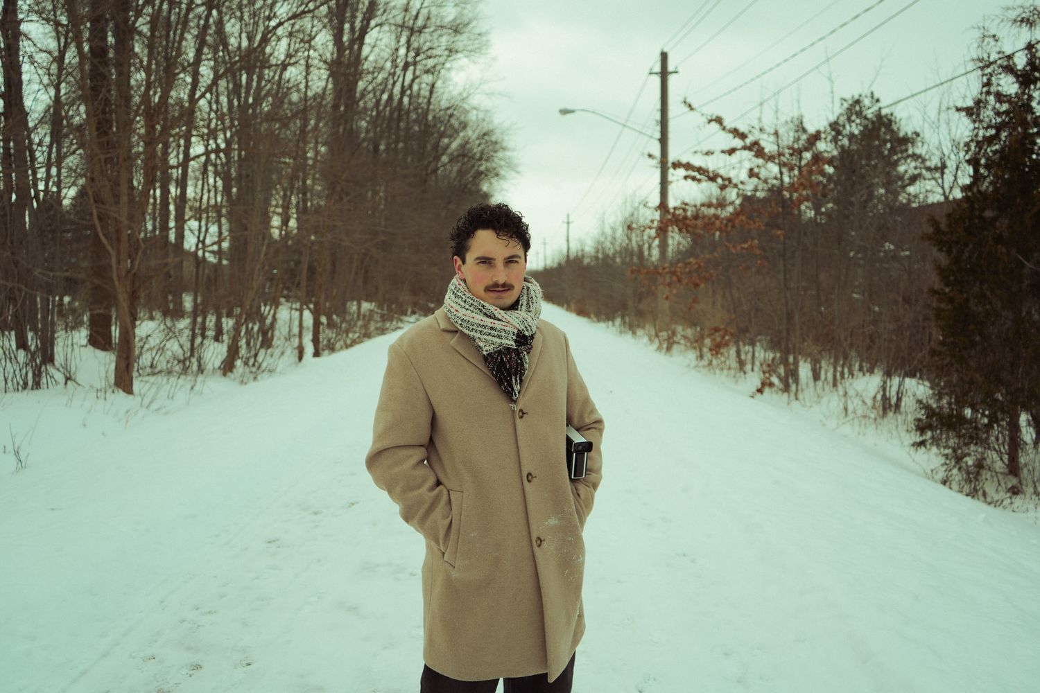 A person walks through a snowy winter landscape wearing a beige coat and black pants.