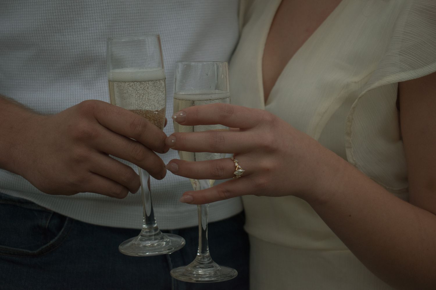 Couple clinking champagne flutes in a toast, woman wearing an engagement ring, celebrating a special occasion.