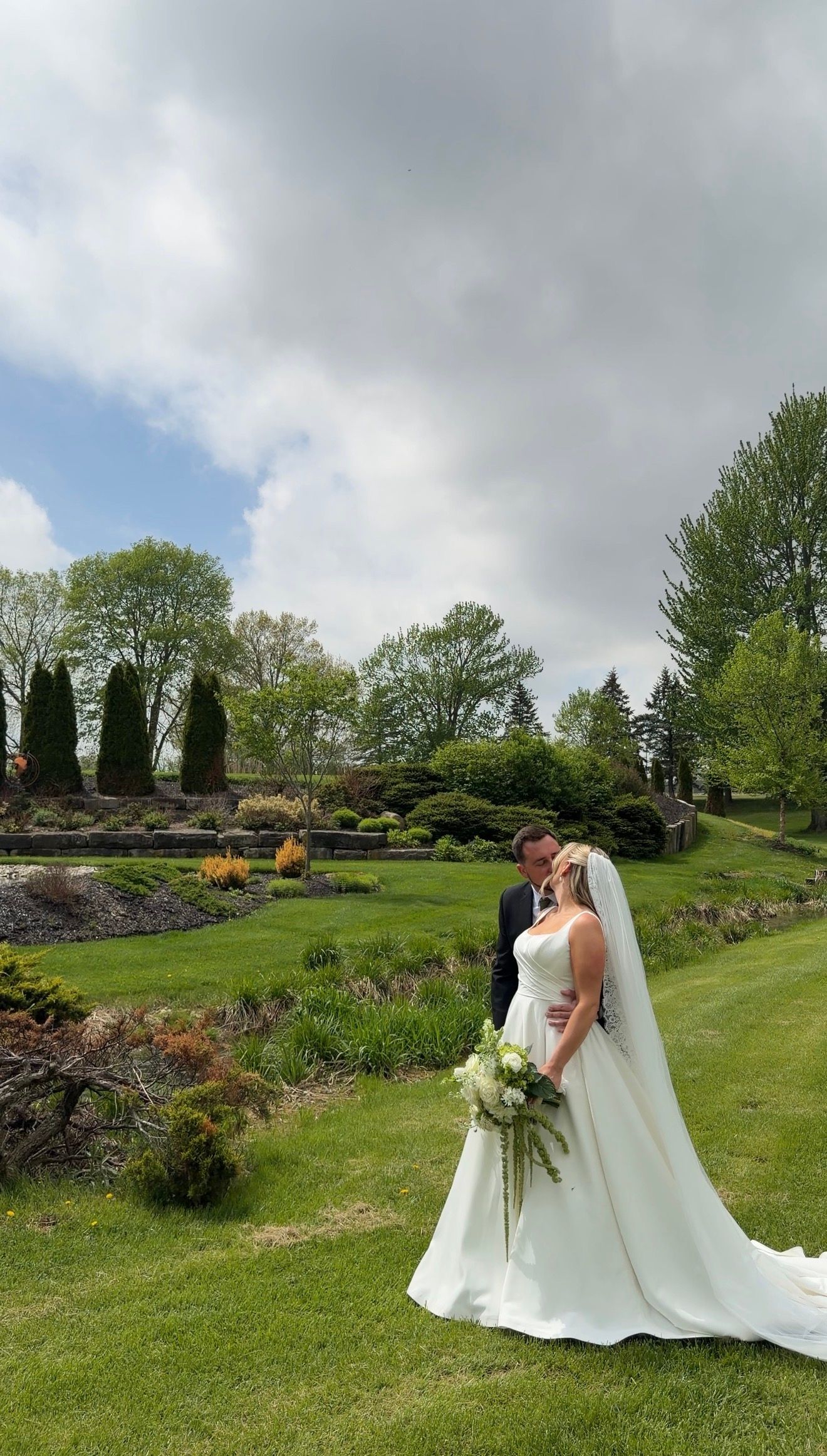 A bride and groom share a romantic moment in a lush garden, with the bride holding a white bouquet on their wedding day.