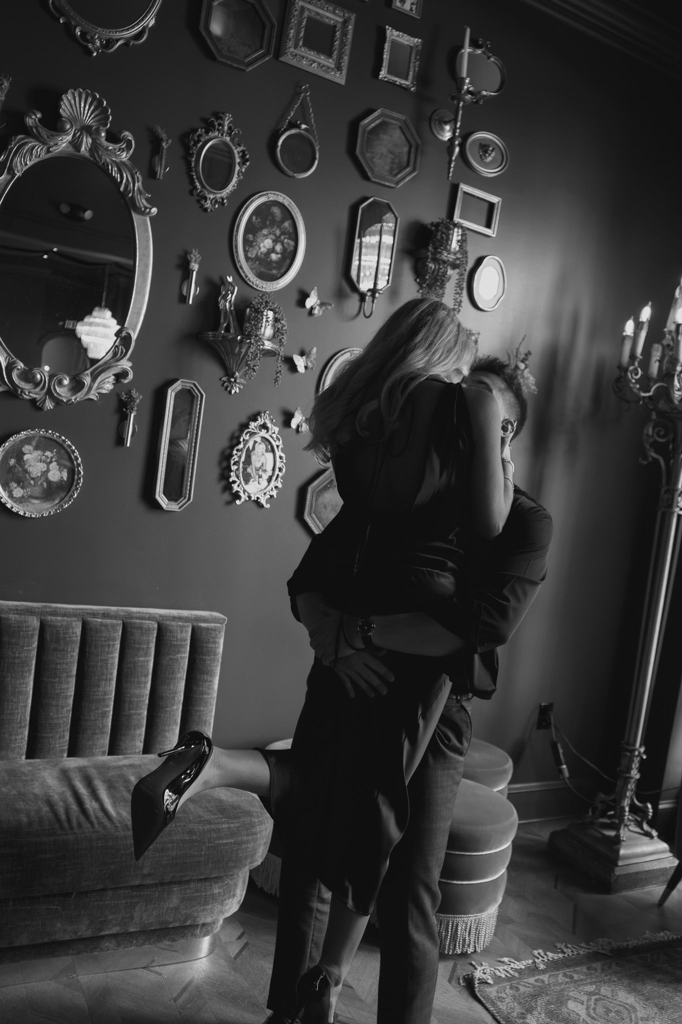 Black and white photo of a couple embracing in an elegant room with ornate mirror wall gallery and vintage decor.