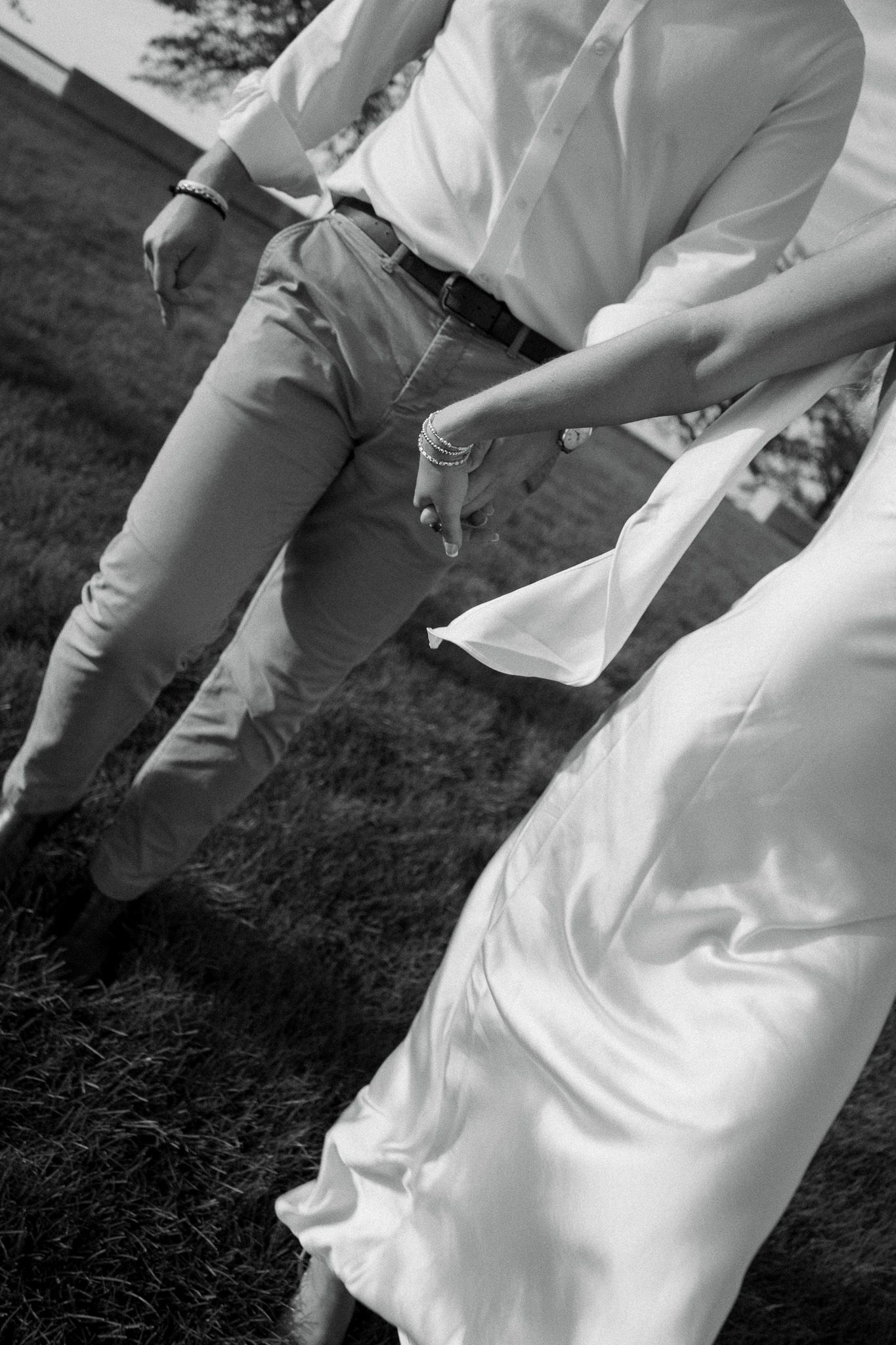 Black and white photo of bride and groom walking hand in hand outdoors, wedding dress flowing gracefully.