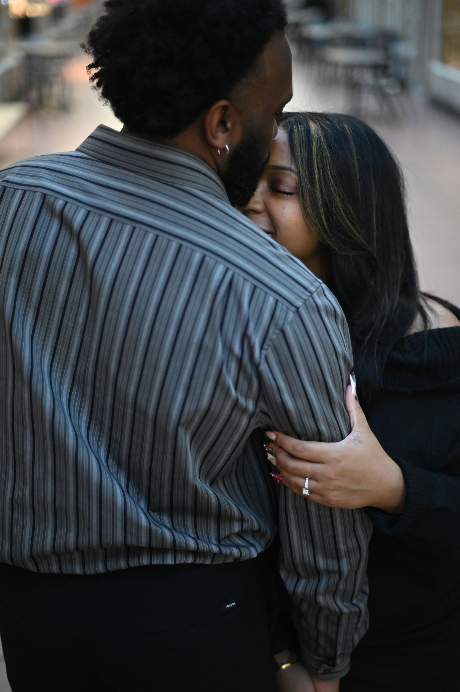 Couple embracing with woman kissing man in striped shirt from behind indoors.