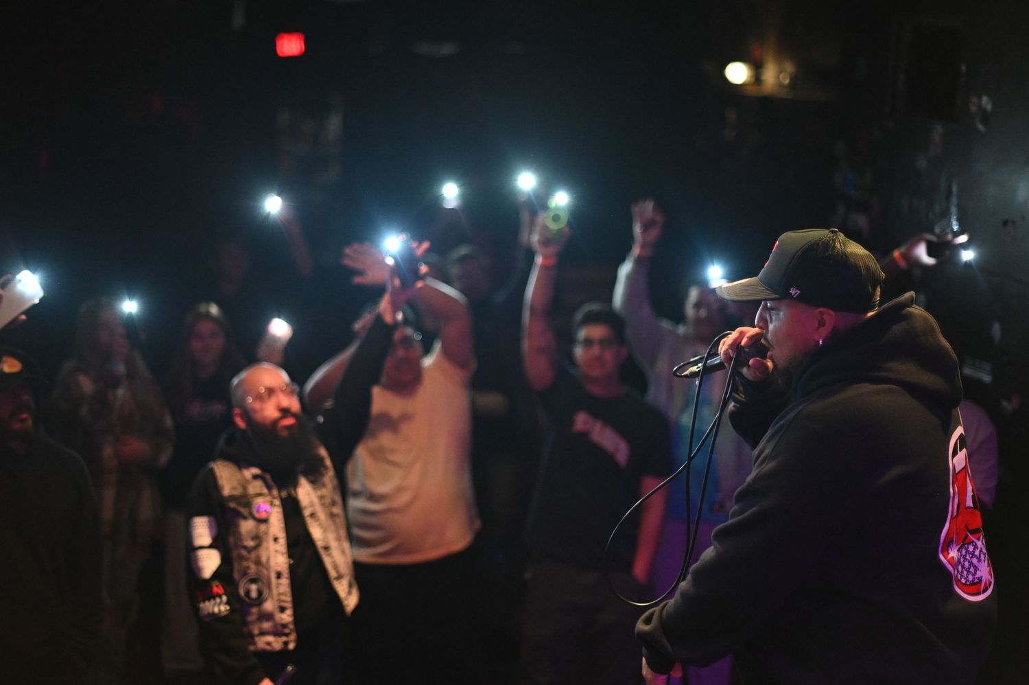 Rapper performing on stage with crowd holding up phone lights at night concert.