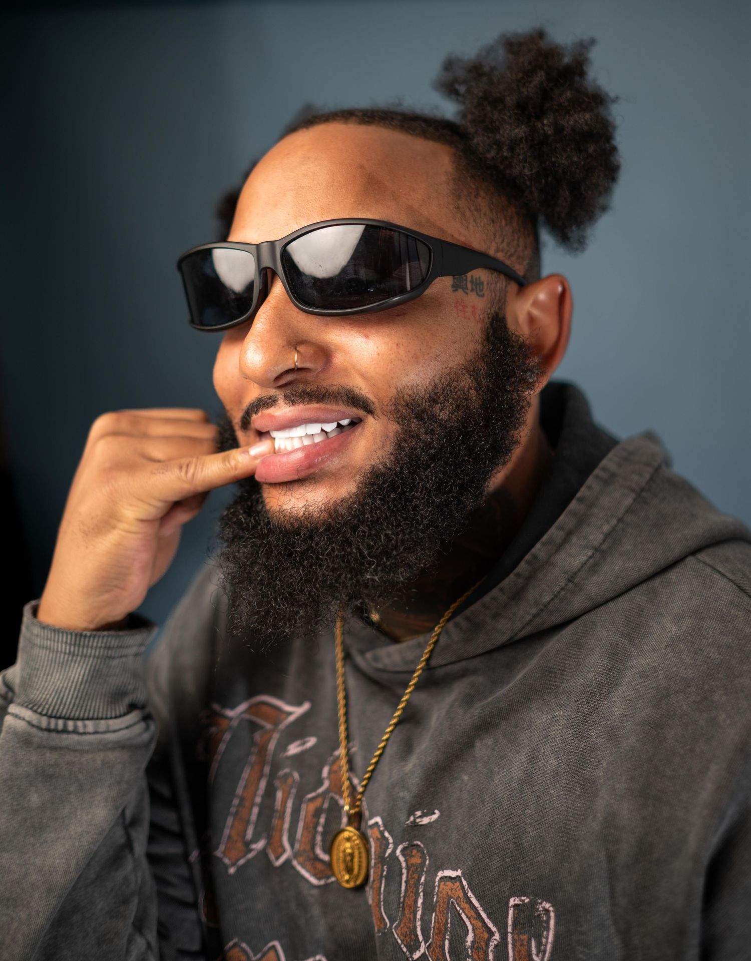 Bearded man in sunglasses and gray hoodie smiles confidently.