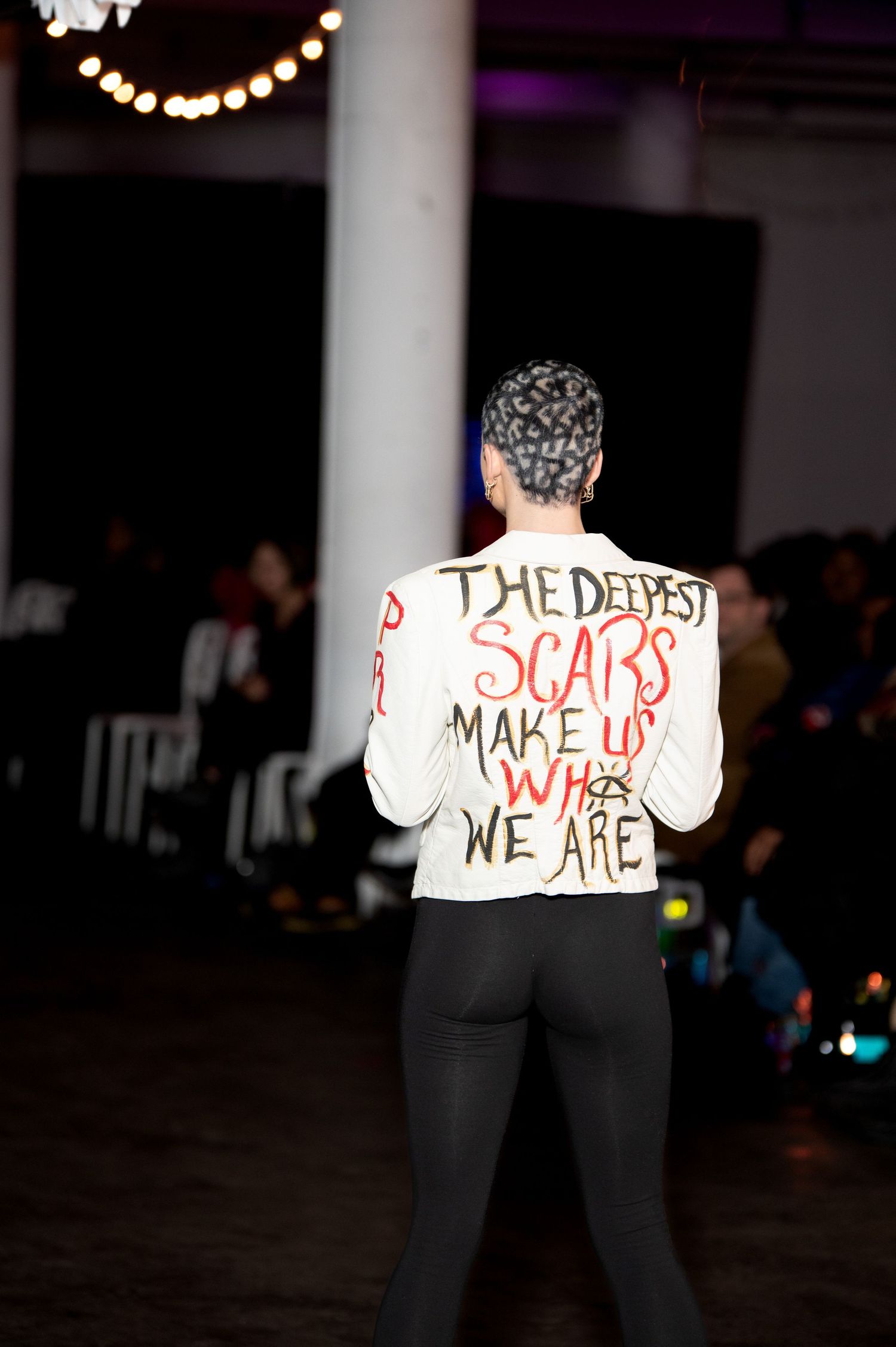 Model displays jacket with text 'The Deepest Scars Make Us Who We Are' on runway.
