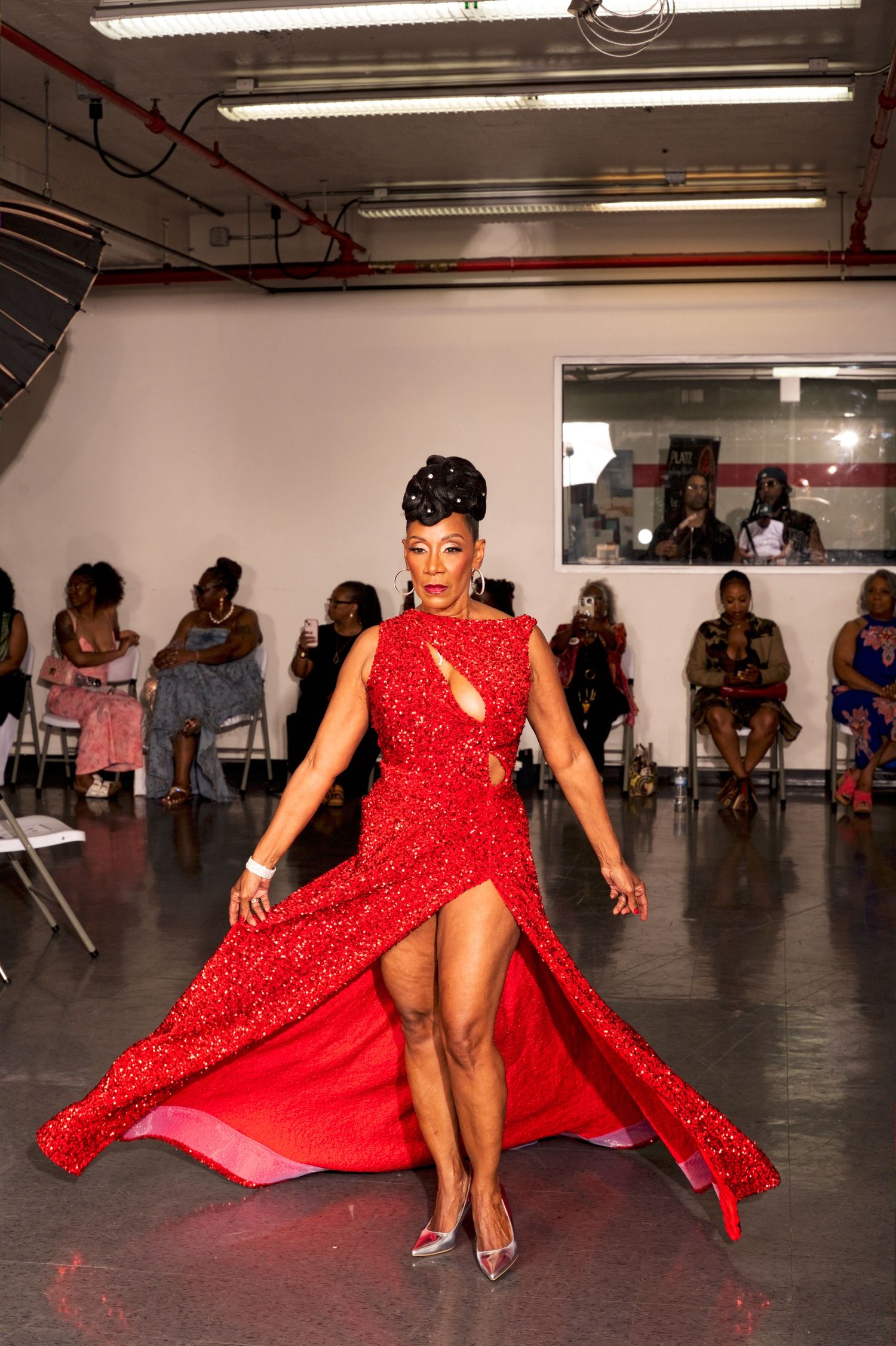Woman in stunning red sequined gown with high slit walks confidently on fashion show runway.