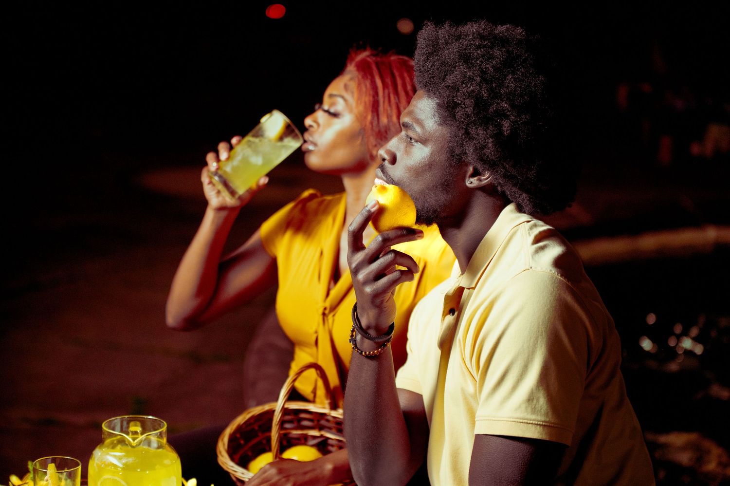 Couple in yellow outfits sharing lemonade outdoors at night.
