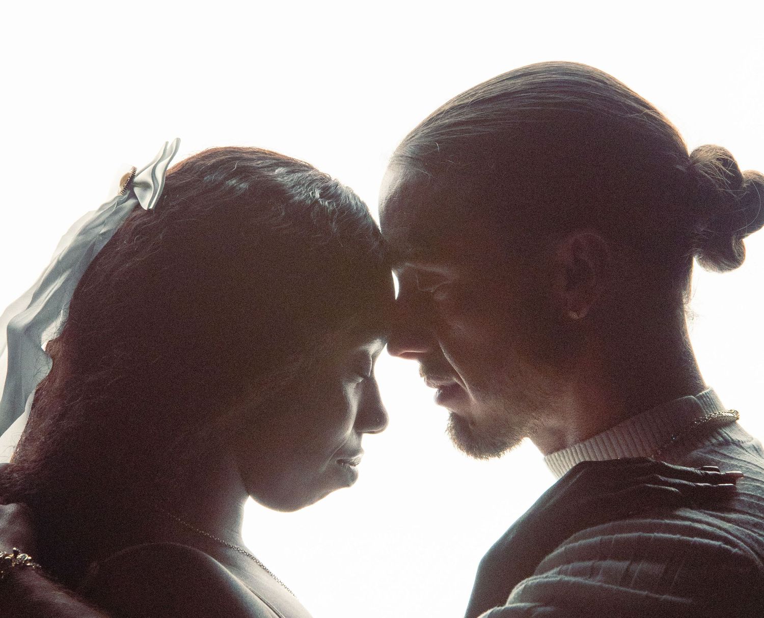Intimate close-up of couple touching foreheads in a tender romantic moment against bright background.