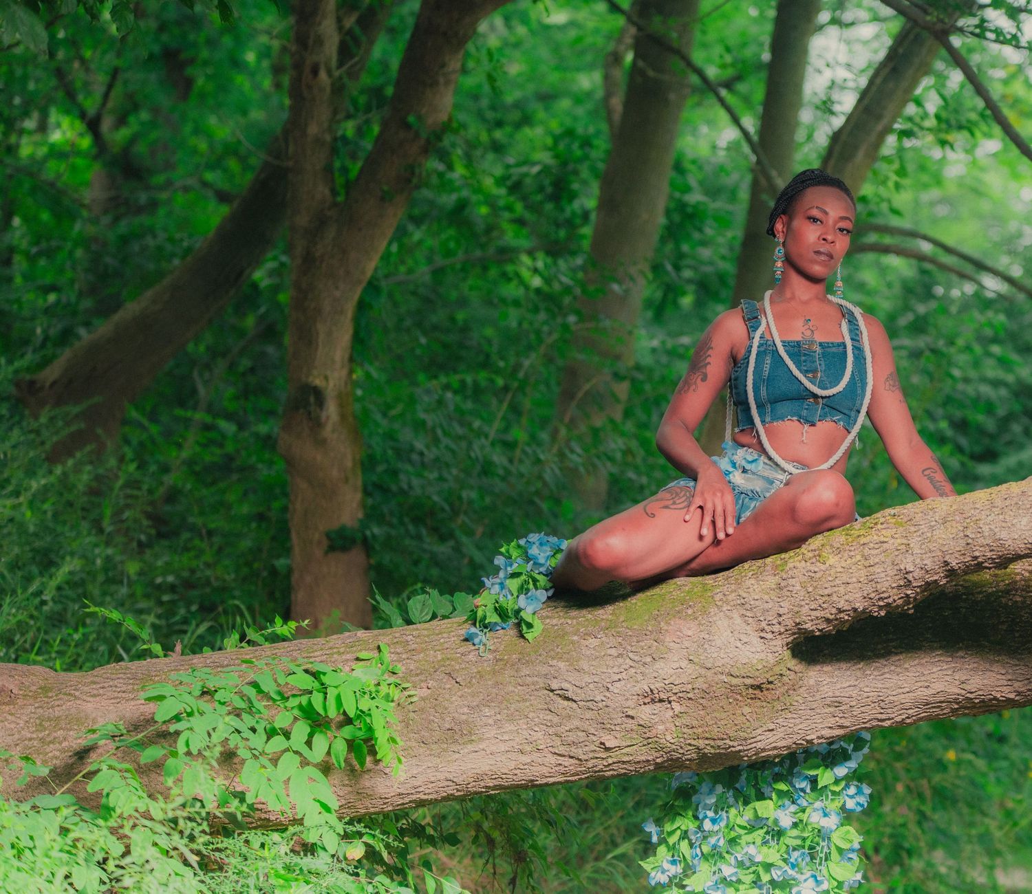 Woman in blue crop top meditates peacefully on fallen tree branch in lush green forest.
