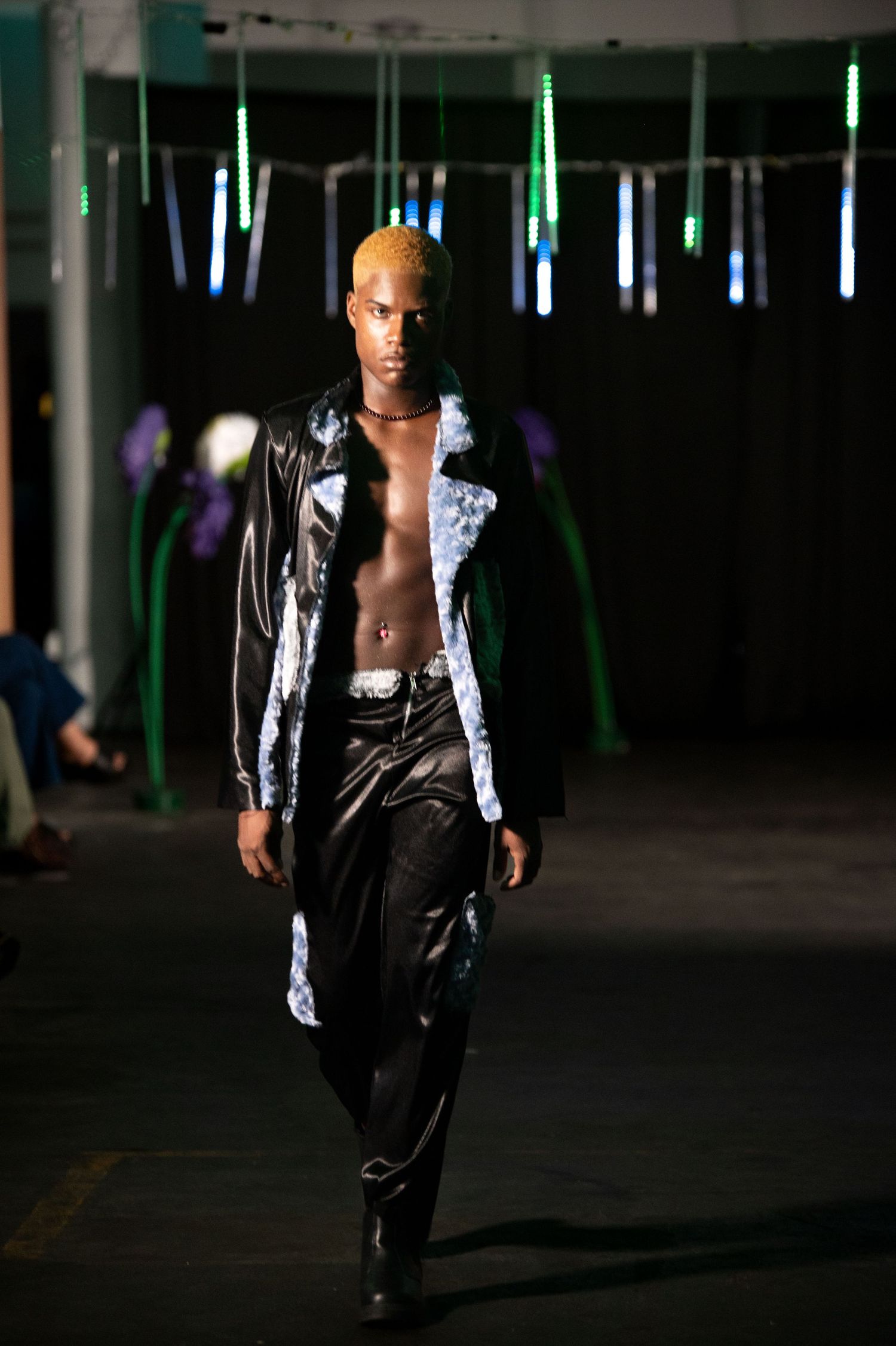 Male model with blonde hair wearing open black leather jacket and pants on fashion runway.