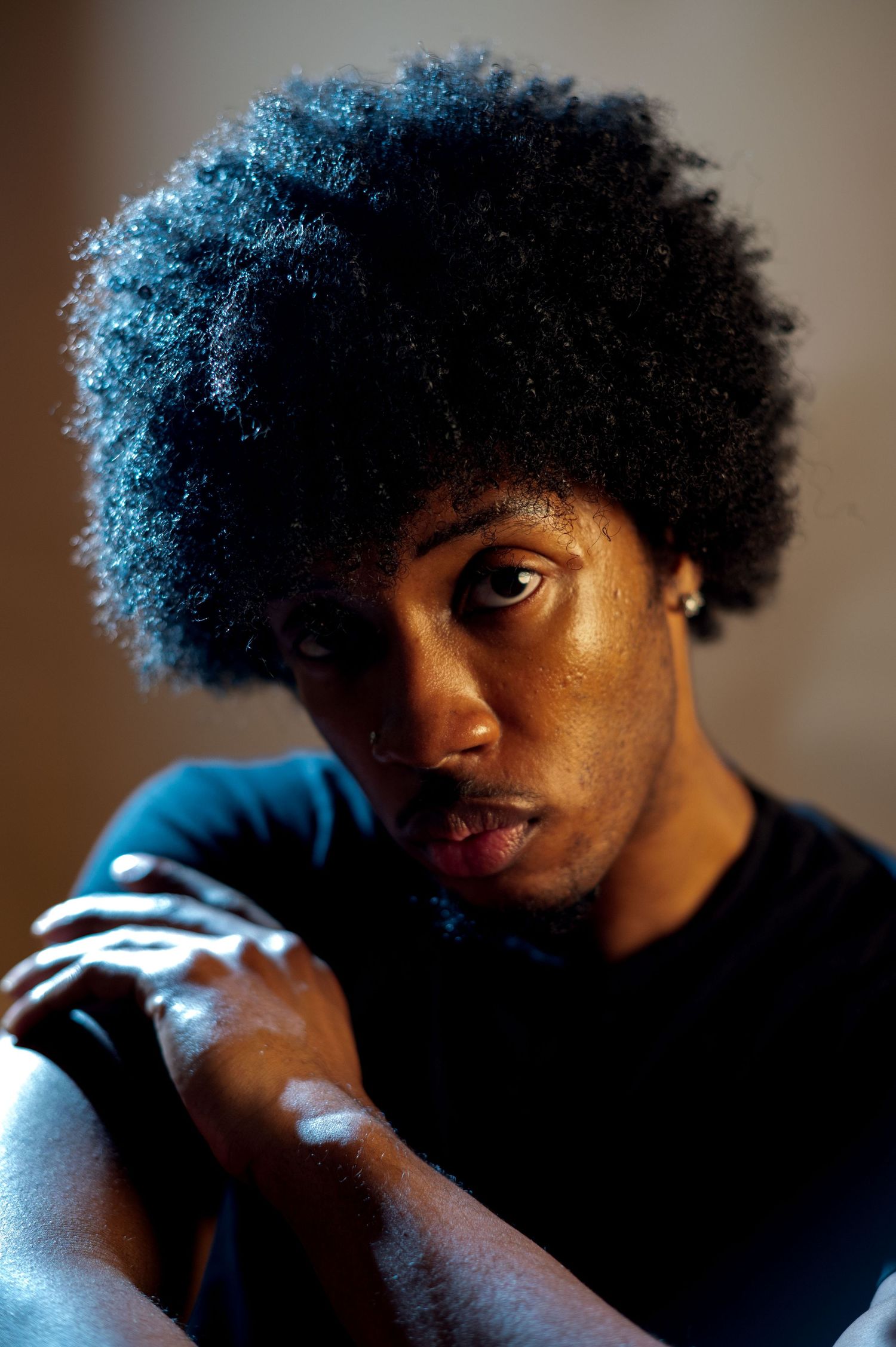 Young man with afro hairstyle poses in dramatic moody lighting.