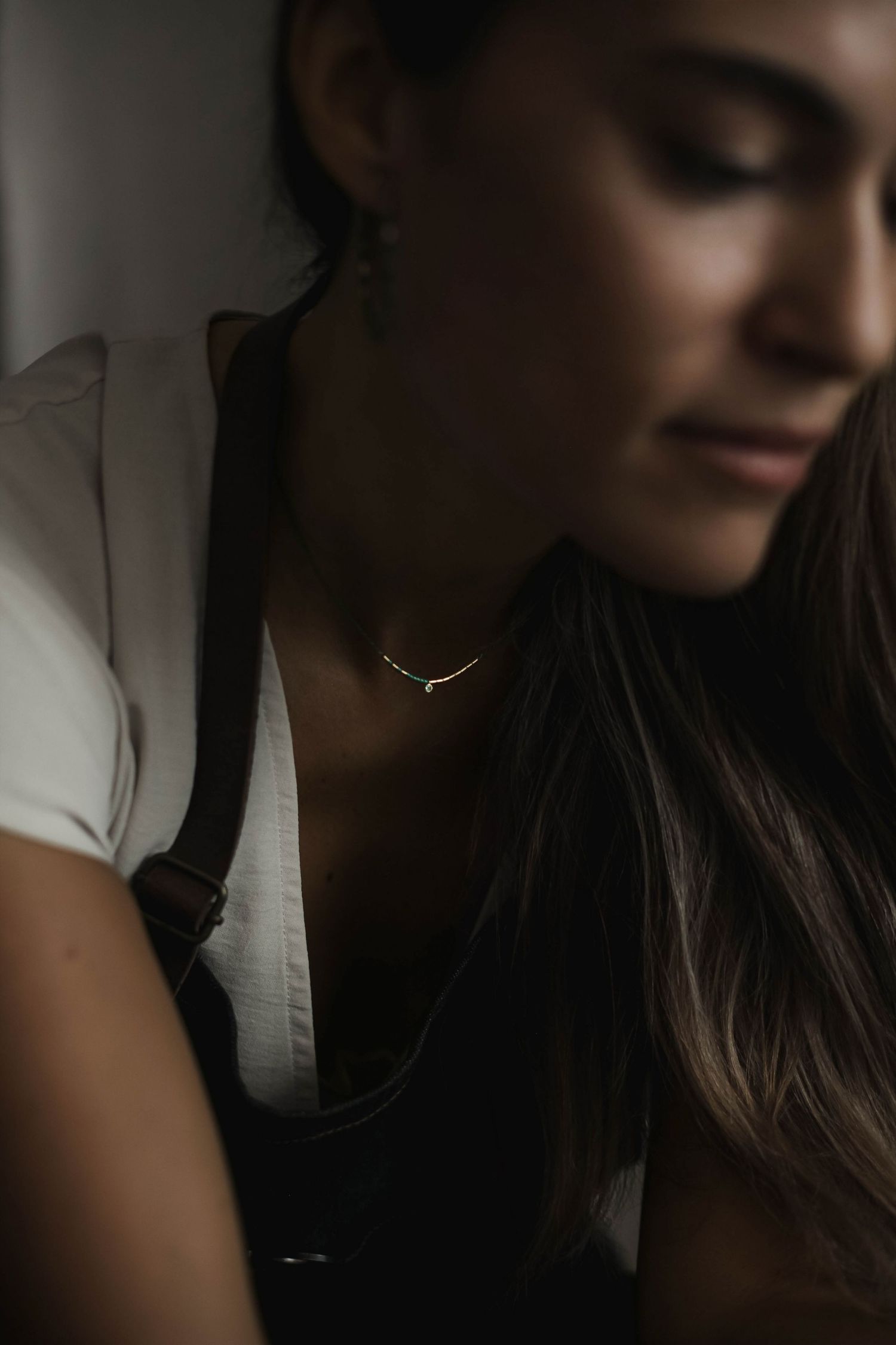 Moody portrait featuring minimal gold necklace and white top in dramatic lighting.