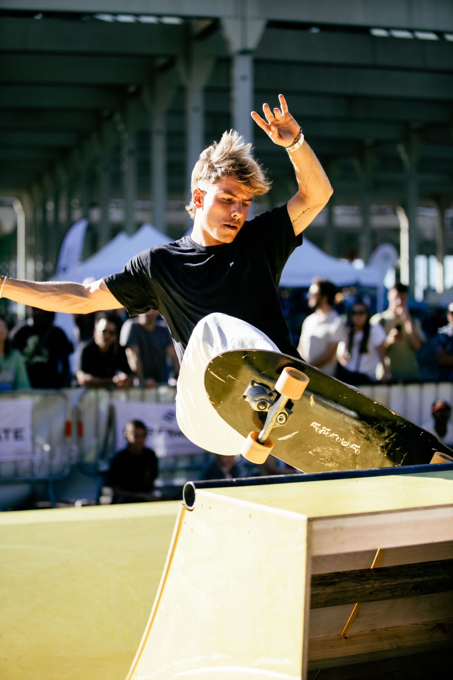 Skateboarder performing aerial trick over wooden ramp in sunlit indoor space.