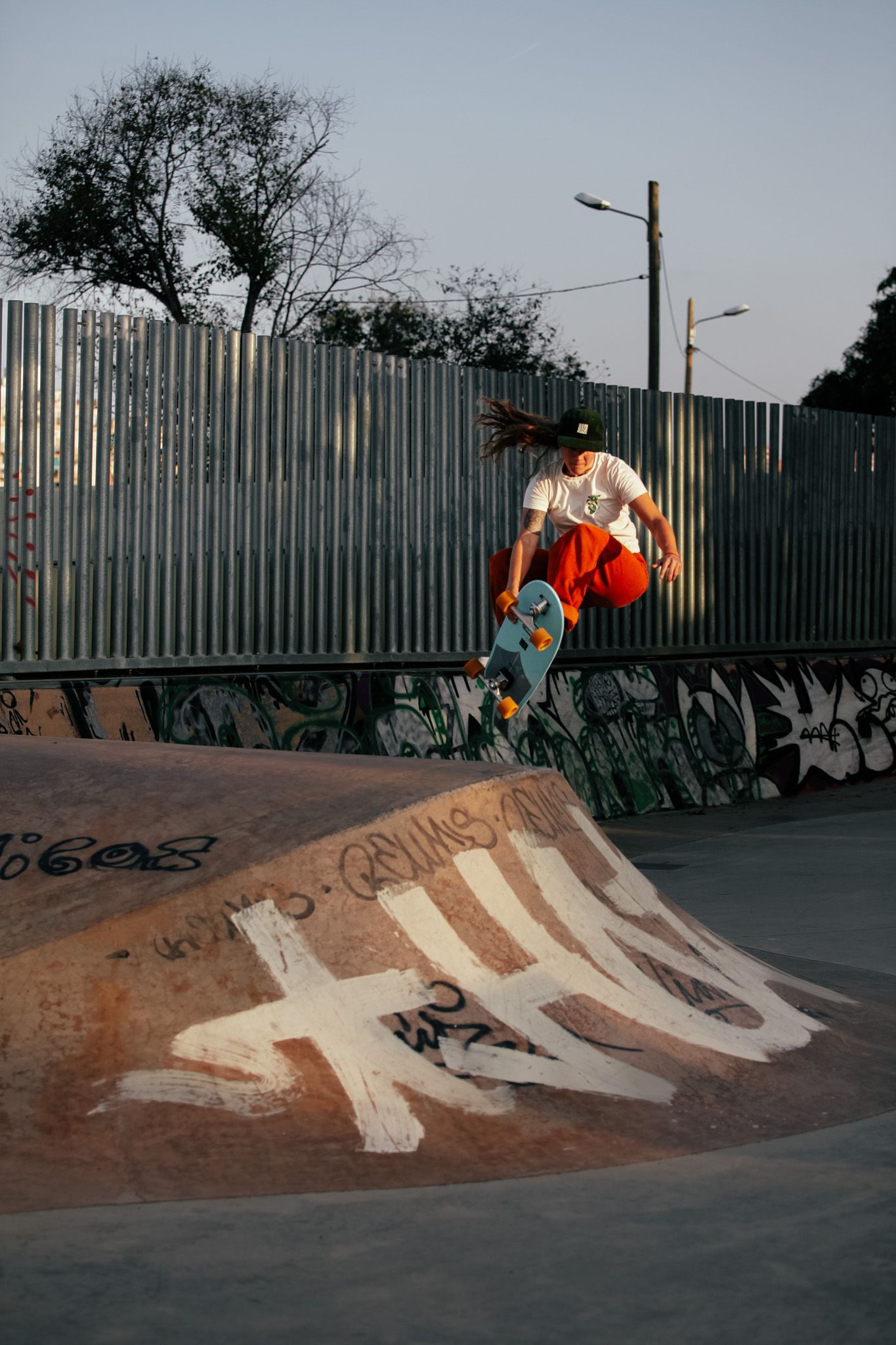 Skateboarder performing an aerial trick at sunset in an urban skate park with graffiti-covered walls.