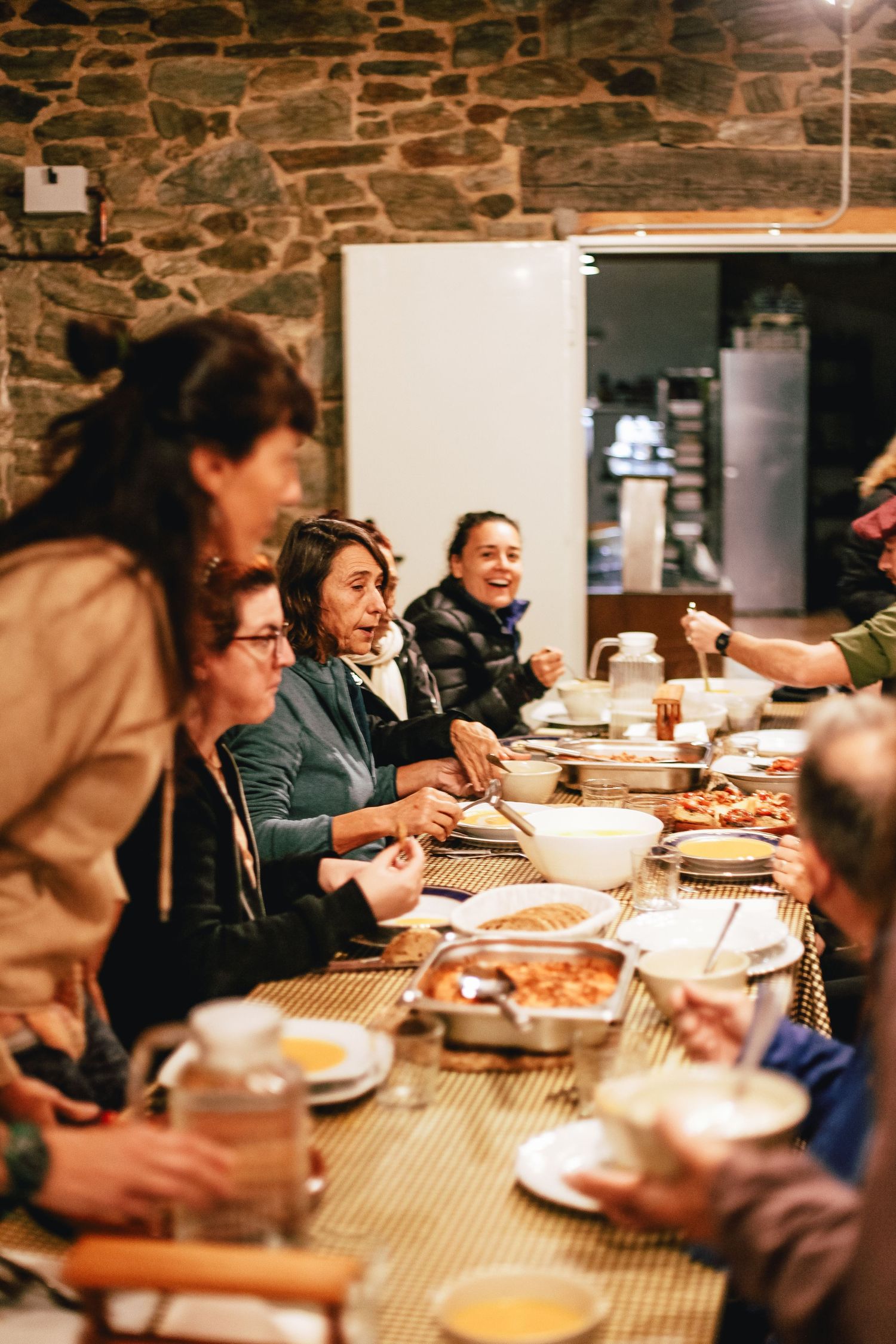 People gathered around a rustic stone-walled dining table sharing a meal together.