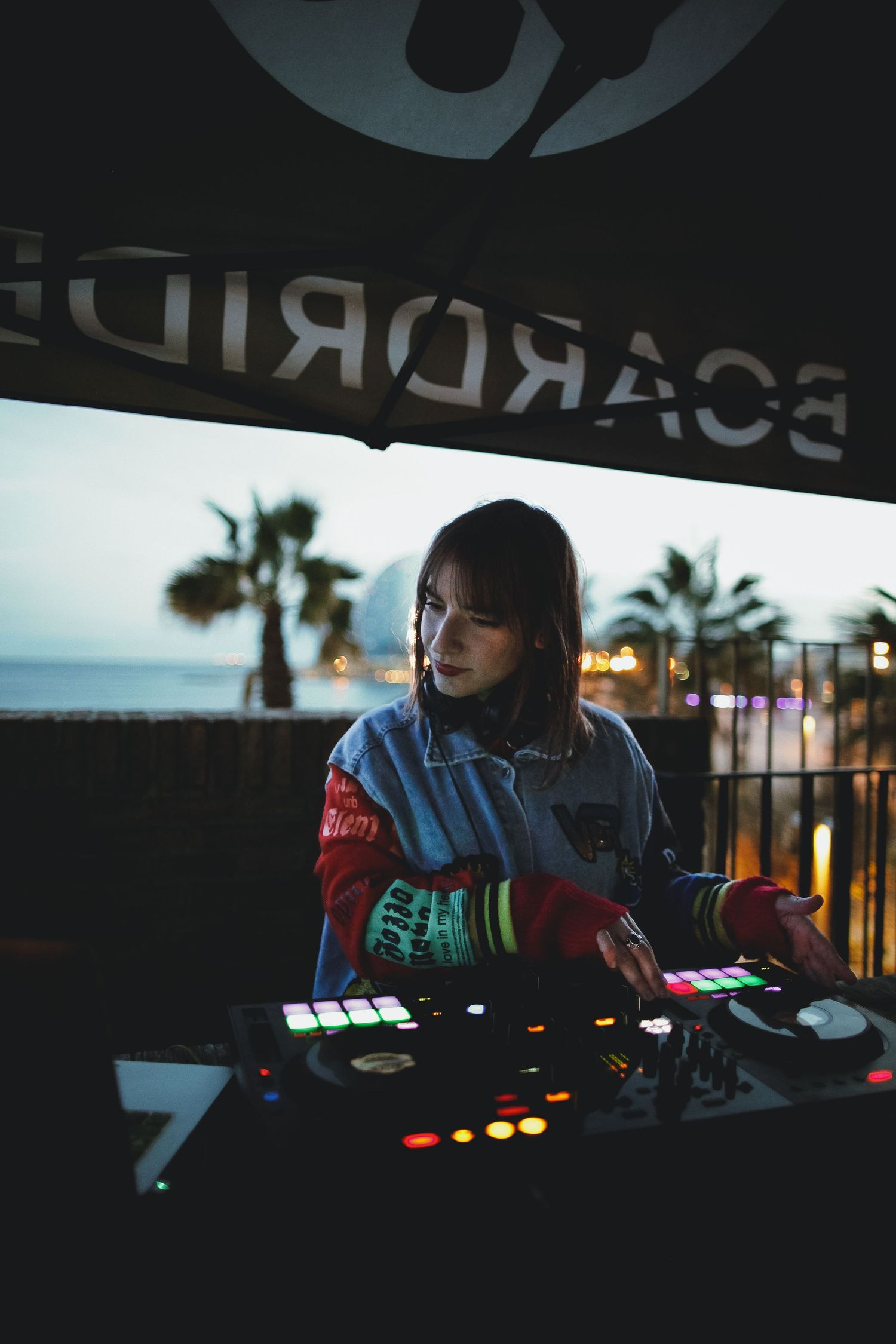 DJ performing behind a dark console with colorful lights and equipment.