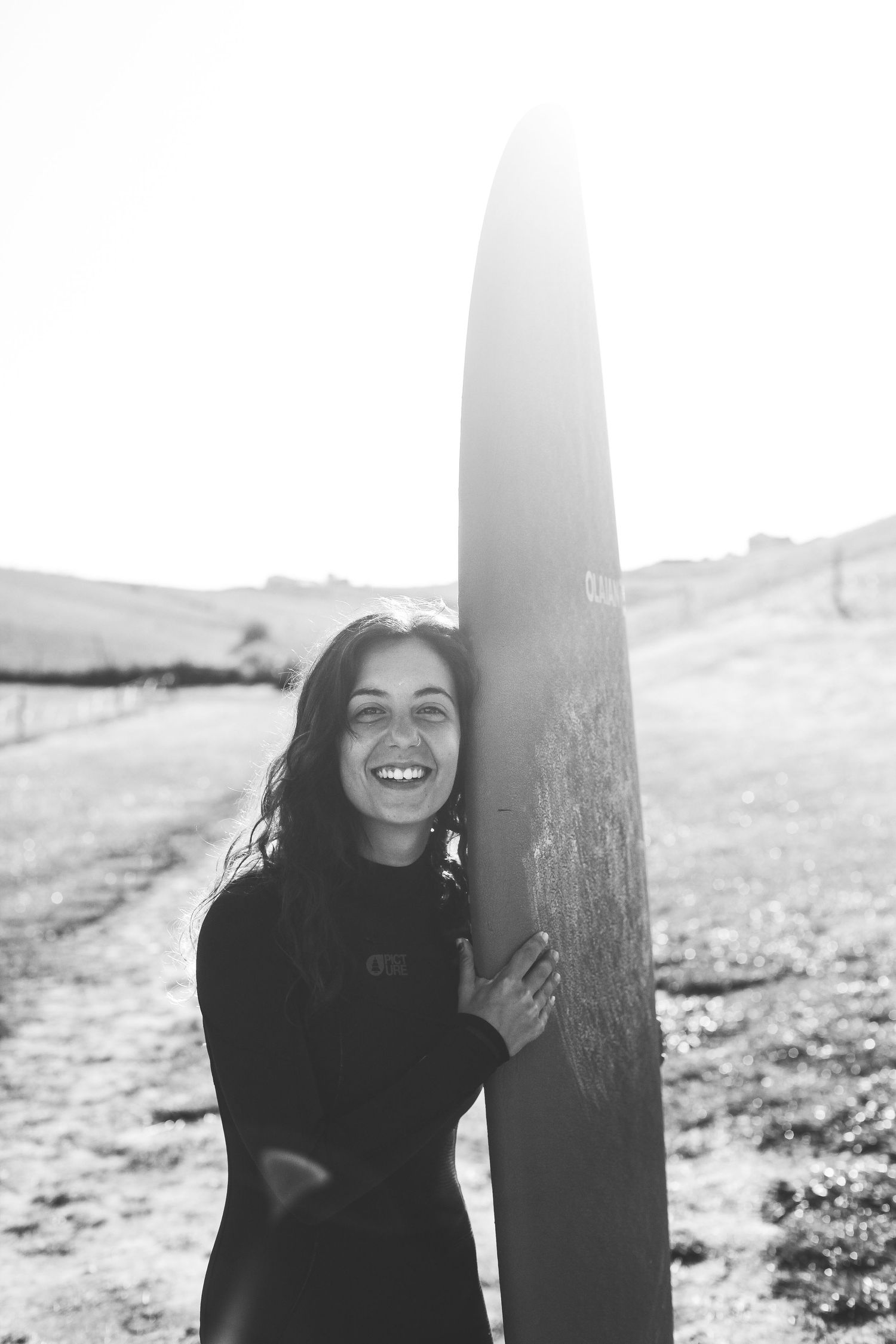 Black and white portrait of someone laughing while leaning against a pole outdoors.