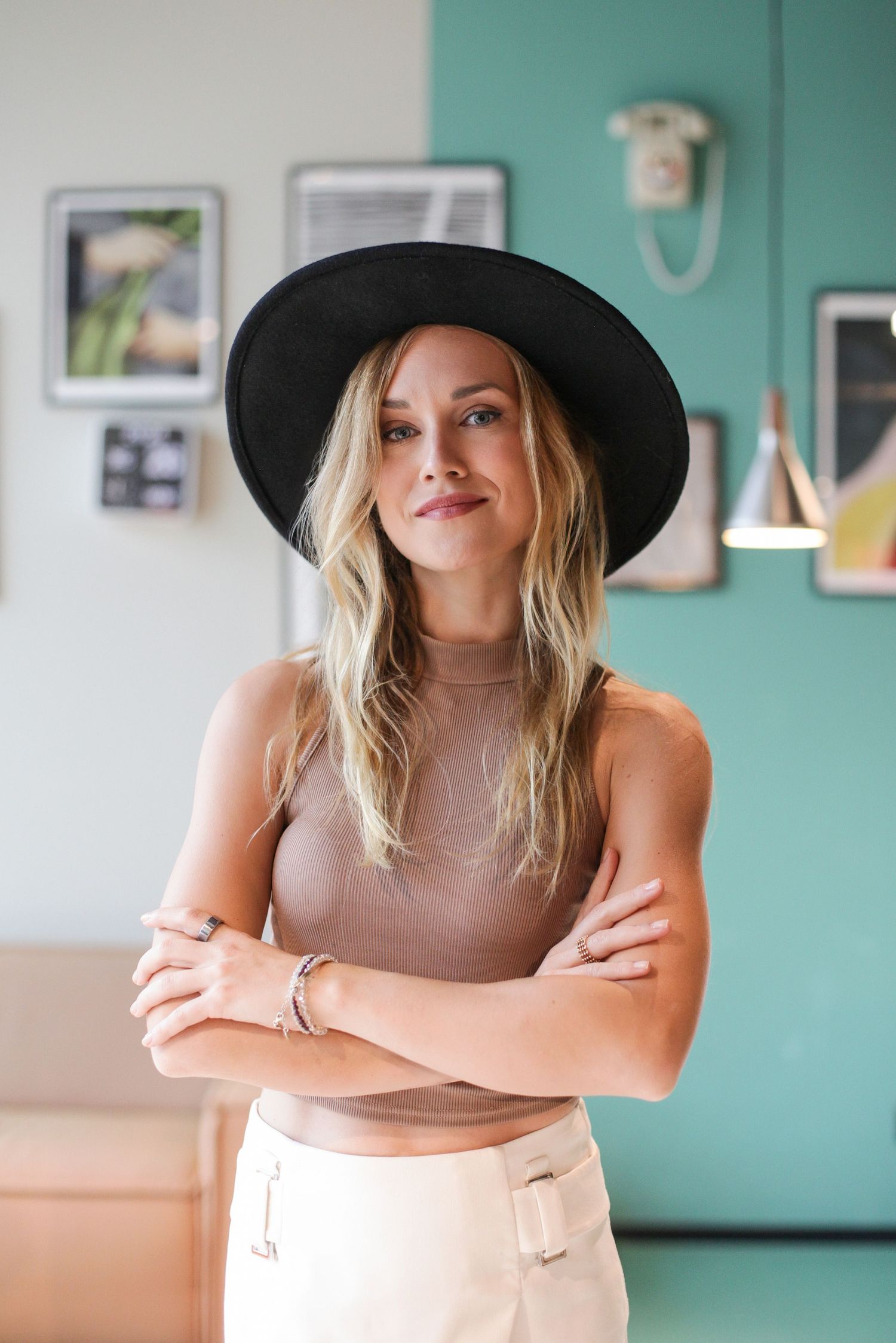 Fashion portrait with black hat and neutral tones against turquoise wall with gallery frames.