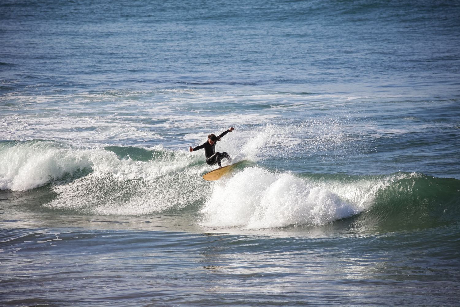Surfer riding a breaking wave on blue ocean water.